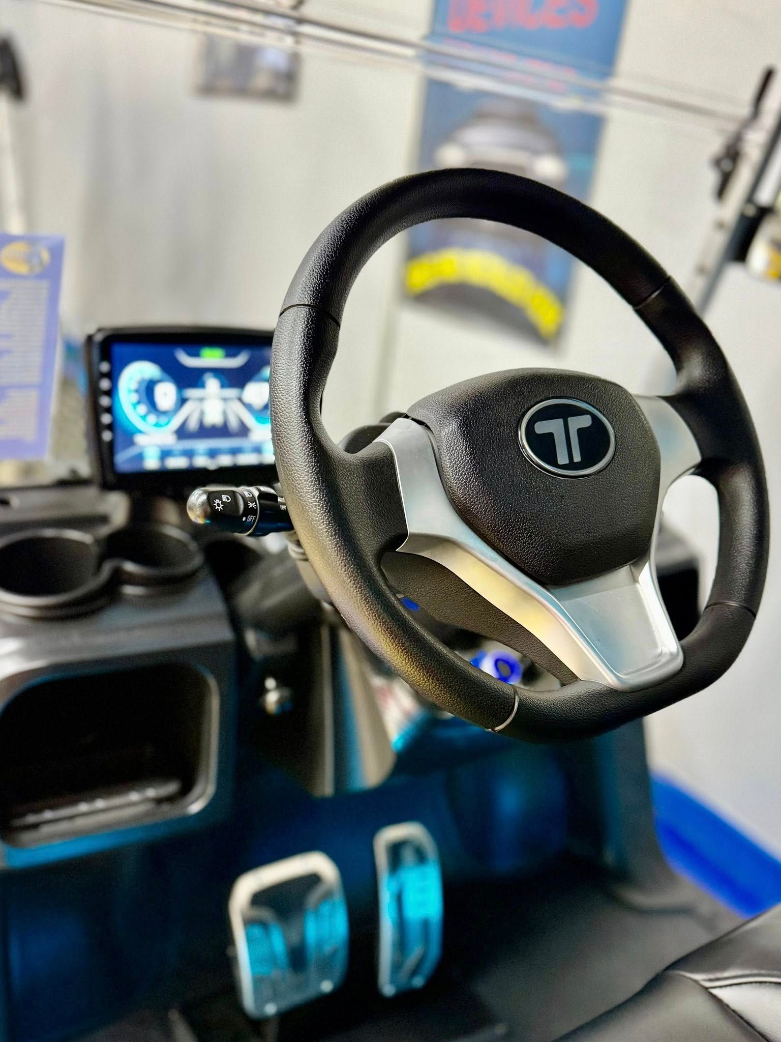 Close-up of a black golf cart interior. Shows steering wheel, digital dashboard, pedals and cup holders.