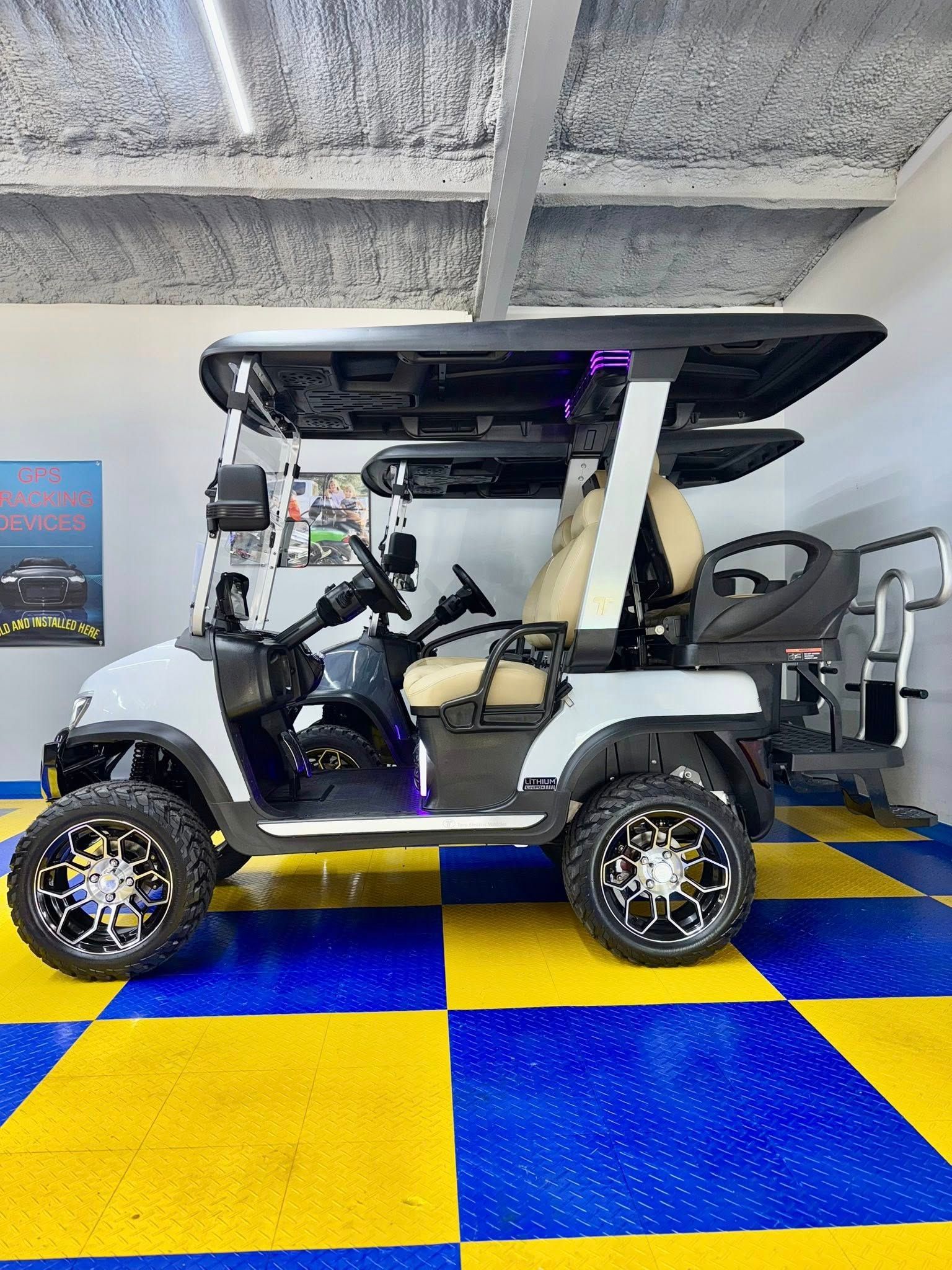 White and black customized golf cart with large wheels, parked on a blue and yellow checkered floor, inside a garage.