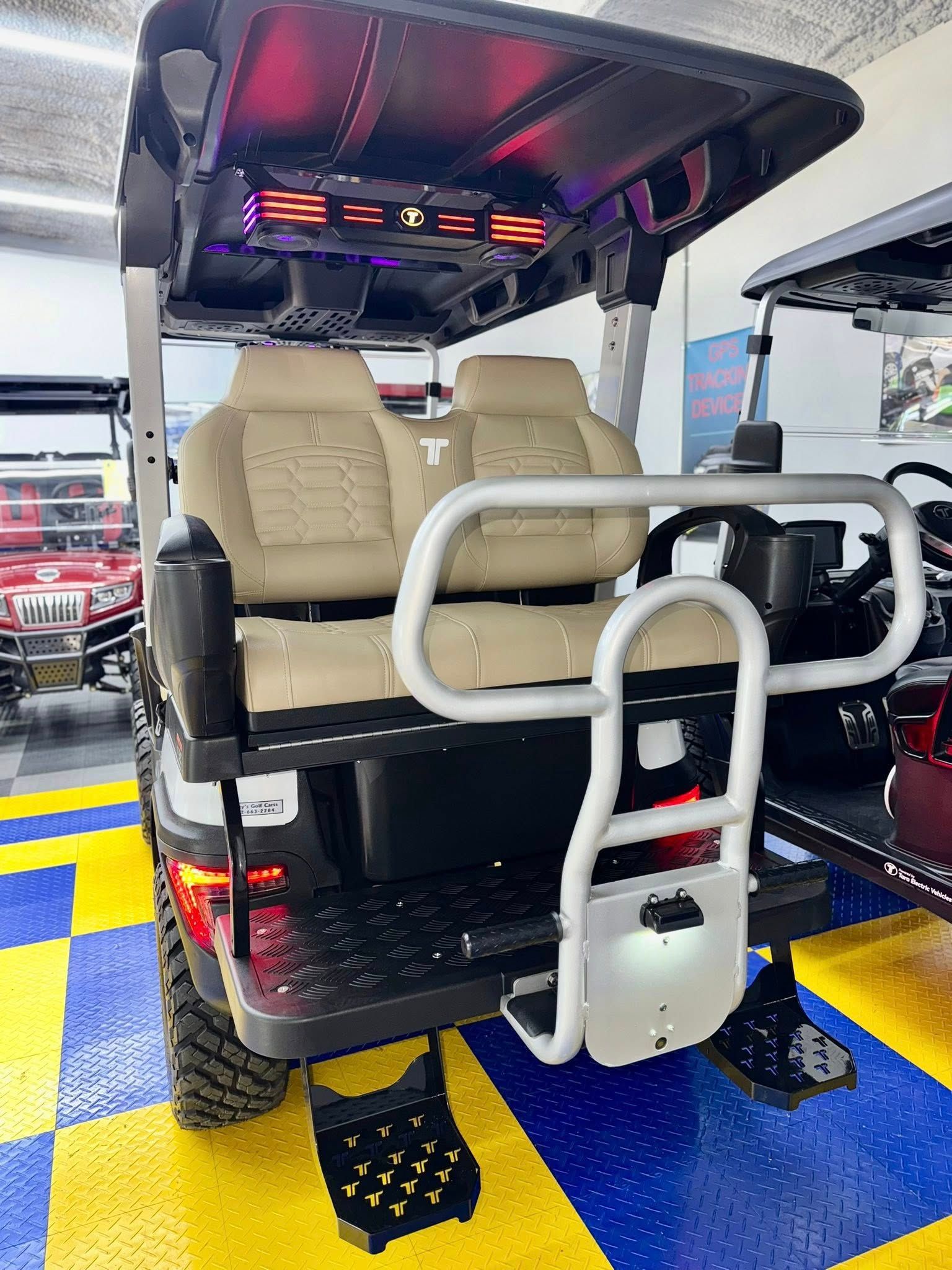 A black golf cart with tan seats, a rear handrail, and off-road tires sits on a blue and yellow checkered floor.