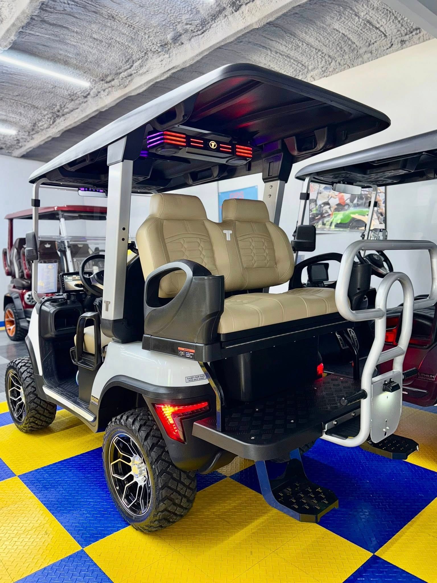 White golf cart with tan seats, black roof, and large off-road tires parked indoors.