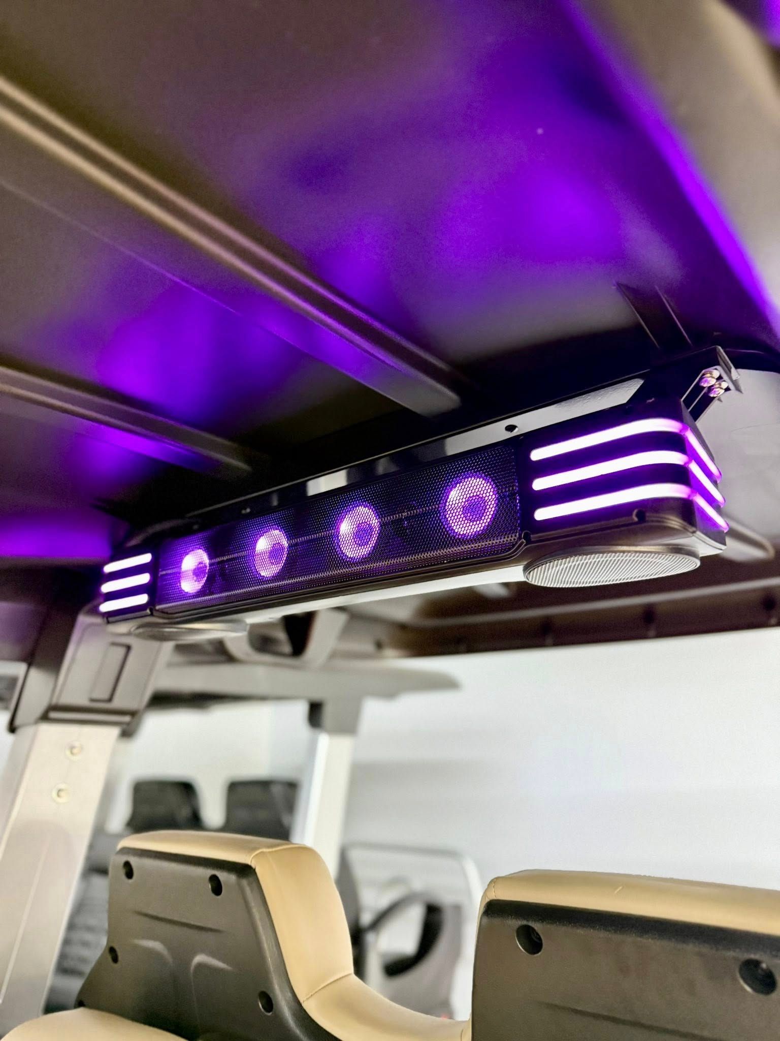 A golf cart's roof-mounted soundbar with vibrant purple LED lighting. The soundbar is black with glowing purple and white accents.
