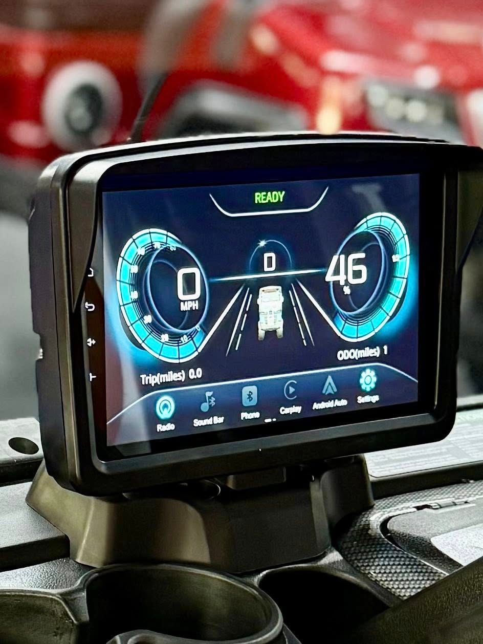 Digital display in a vehicle showing speed and driving information with a red vehicle visible in the blurred background.
