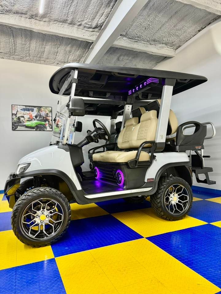 White golf cart with black roof and custom wheels, lit by purple lights, parked on a checkered yellow and blue floor.