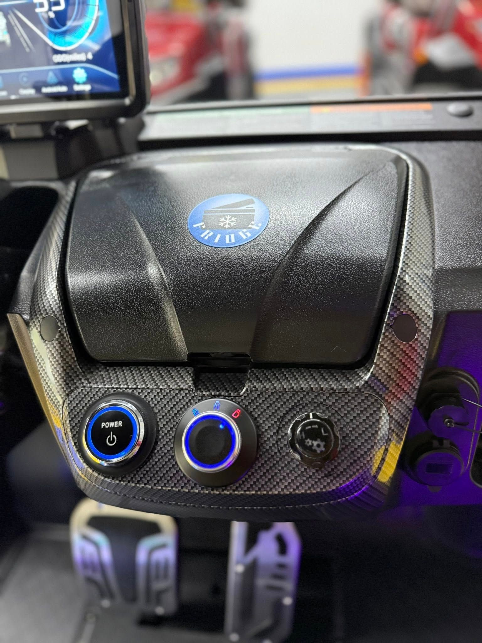 Close-up of a car's dashboard with three illuminated blue buttons. The dashboard is black with a carbon fiber pattern.