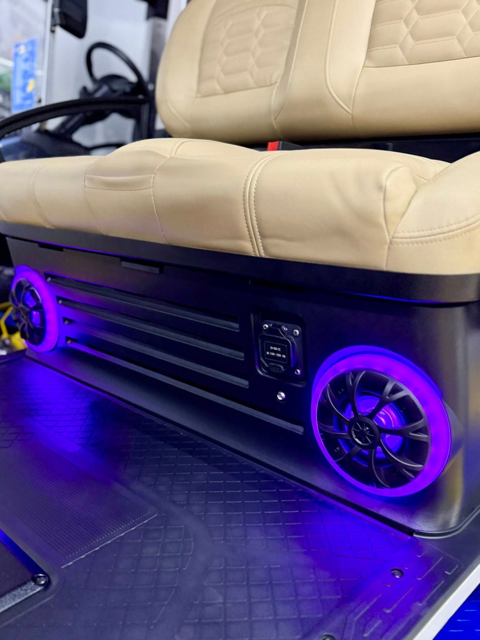 Golf cart with a tan seat and under-seat speaker system illuminated with purple lights. Black accents.