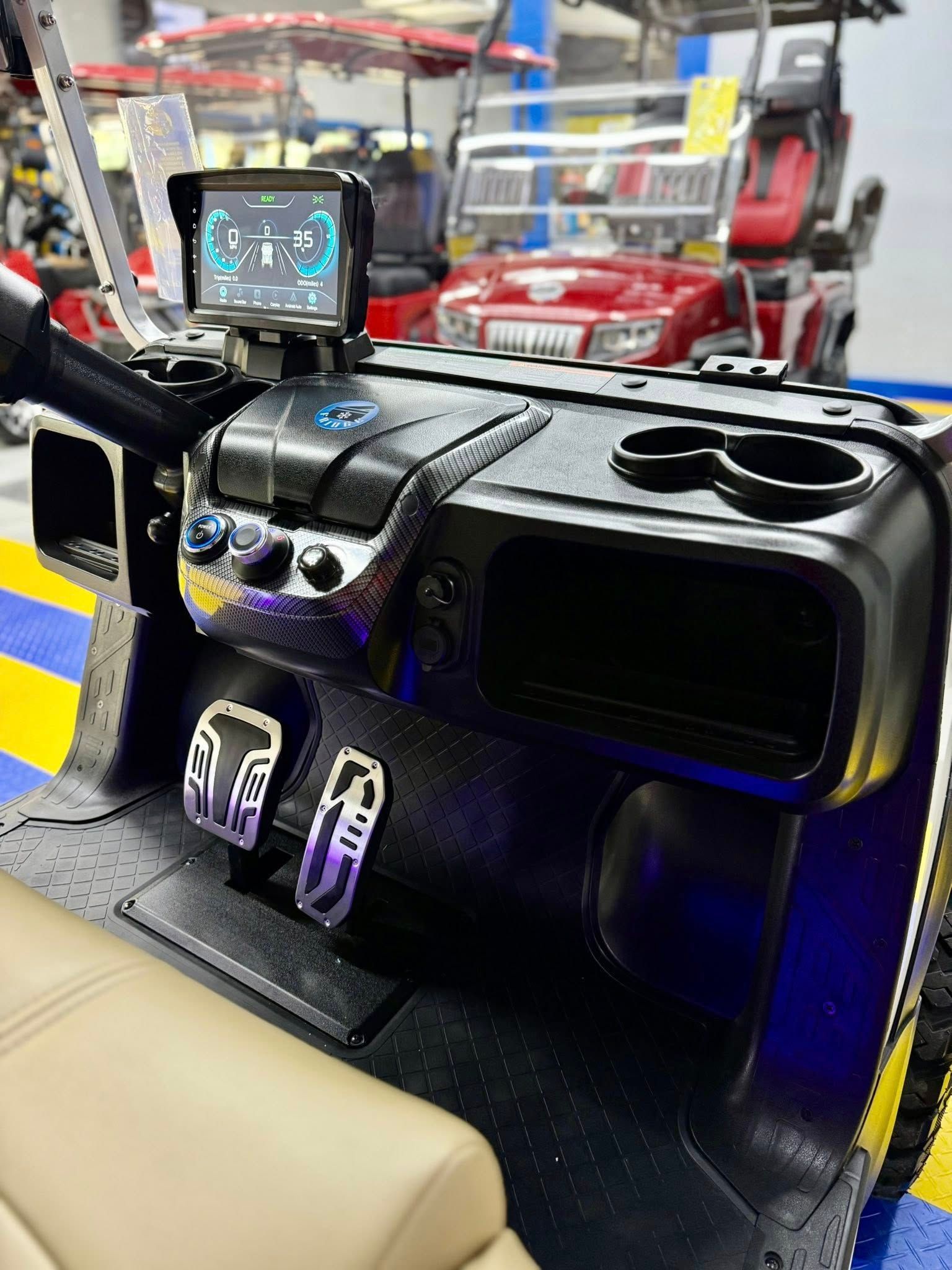 Golf cart dashboard with a digital display, cup holders, and stylish pedals. The interior is black and blue, with tan seating visible.
