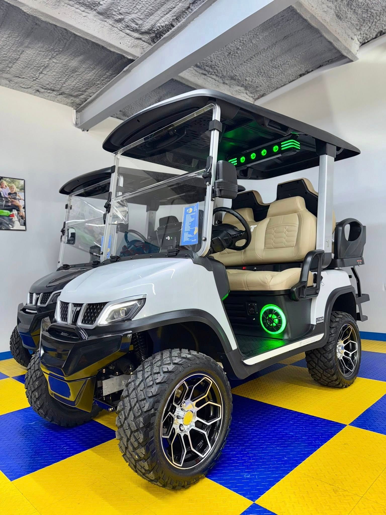 White and gray custom golf cart with black trim, off-road tires, and interior lighting, parked on a blue and yellow checkered floor.