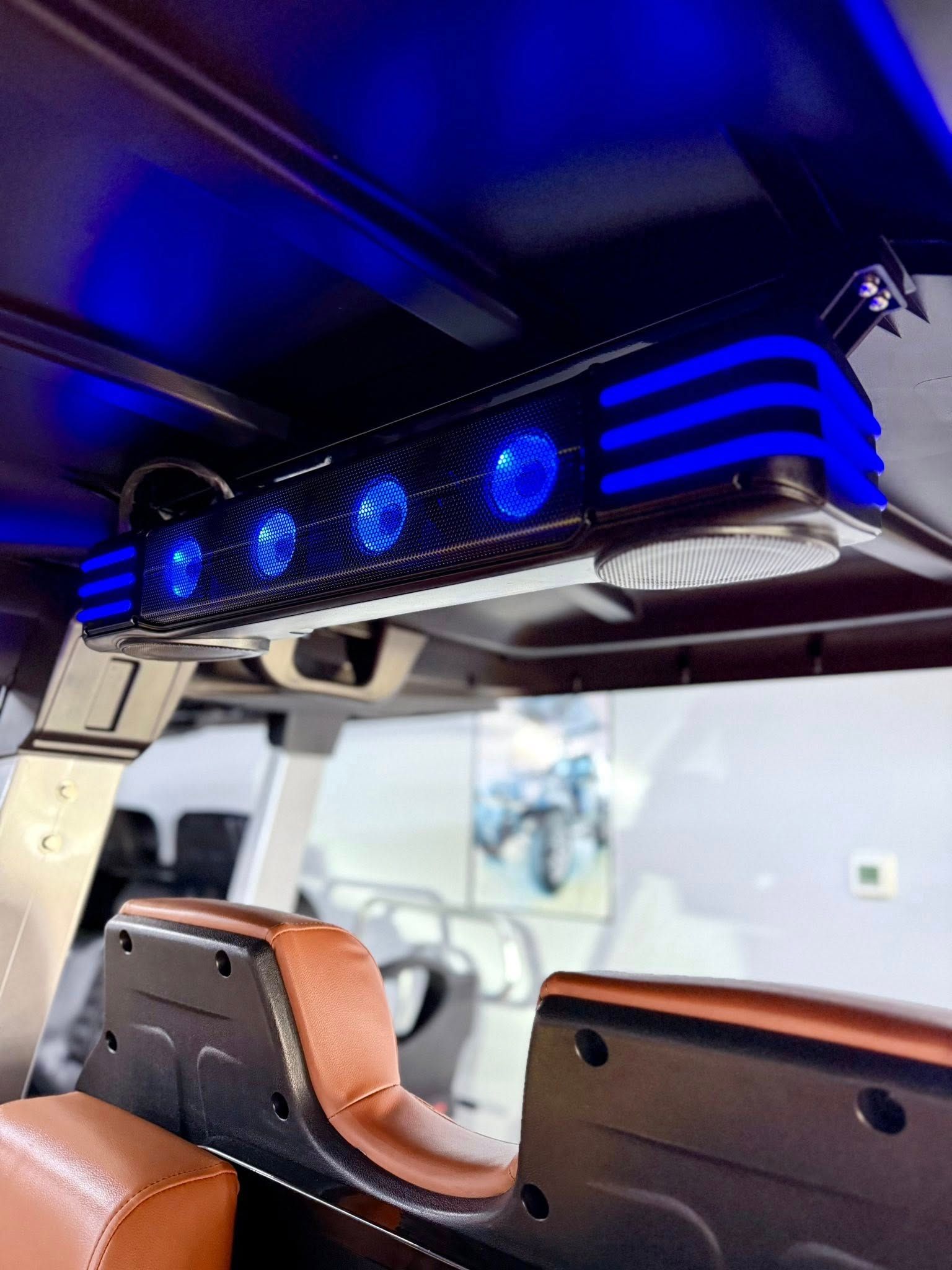 Blue LED soundbar mounted on a golf cart roof, above brown seats.