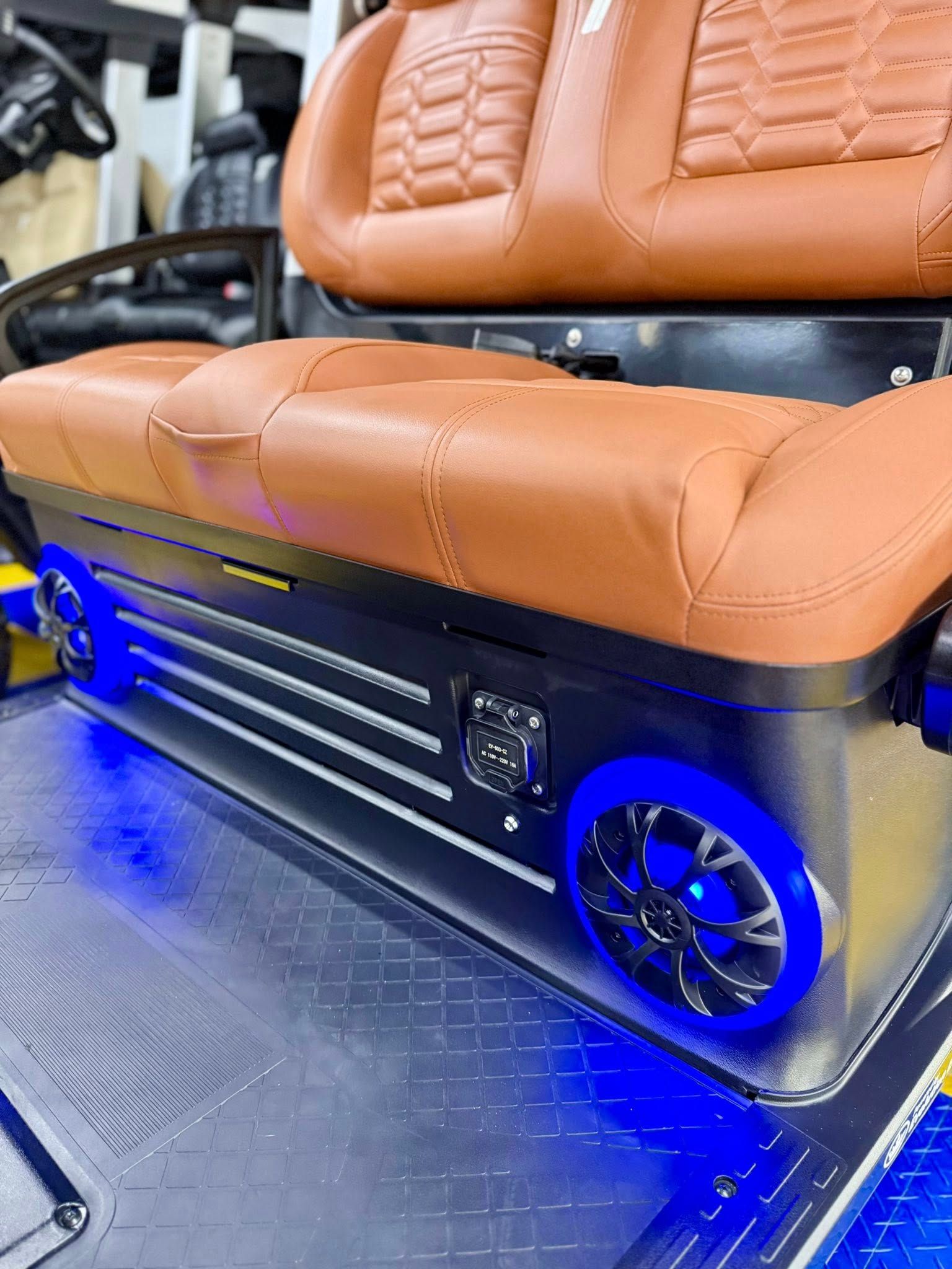 A custom golf cart seat with brown leather upholstery, black accents, blue LED lights, and speakers.