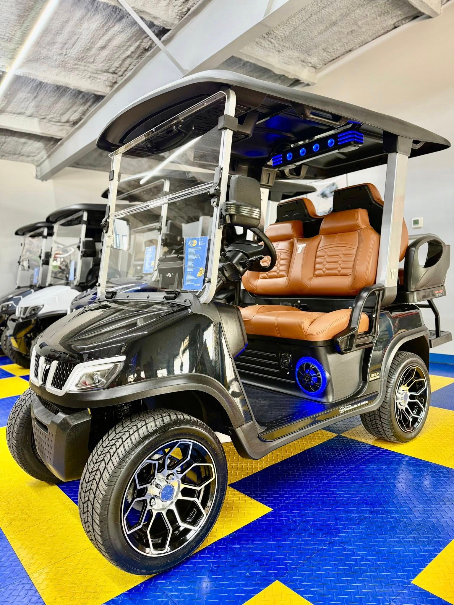 Black golf cart with brown leather seats, custom wheels, and blue undercarriage lighting, displayed indoors.