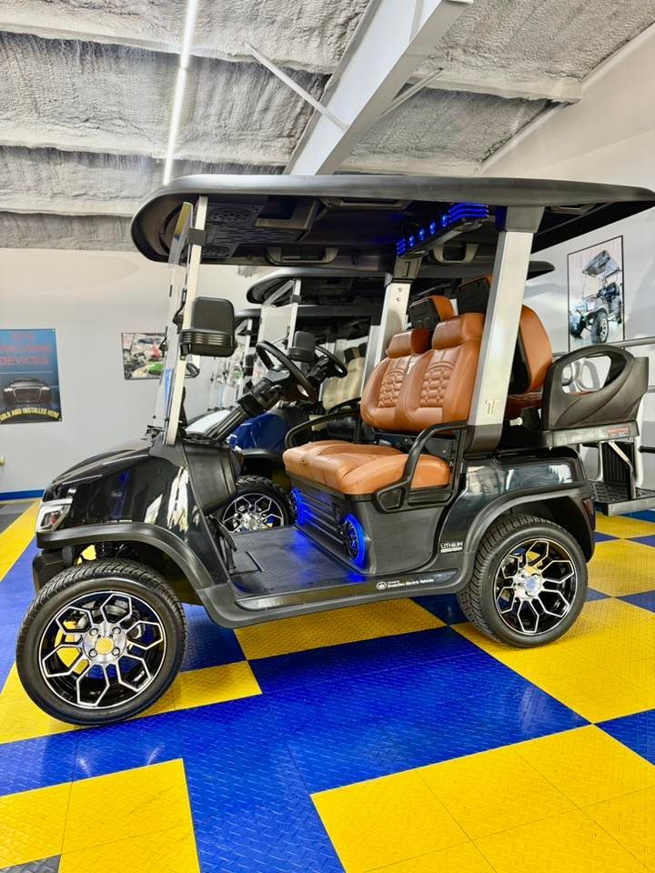 Black golf cart with brown leather seats, custom wheels, and LED lighting in a showroom with blue and yellow checkered floor.