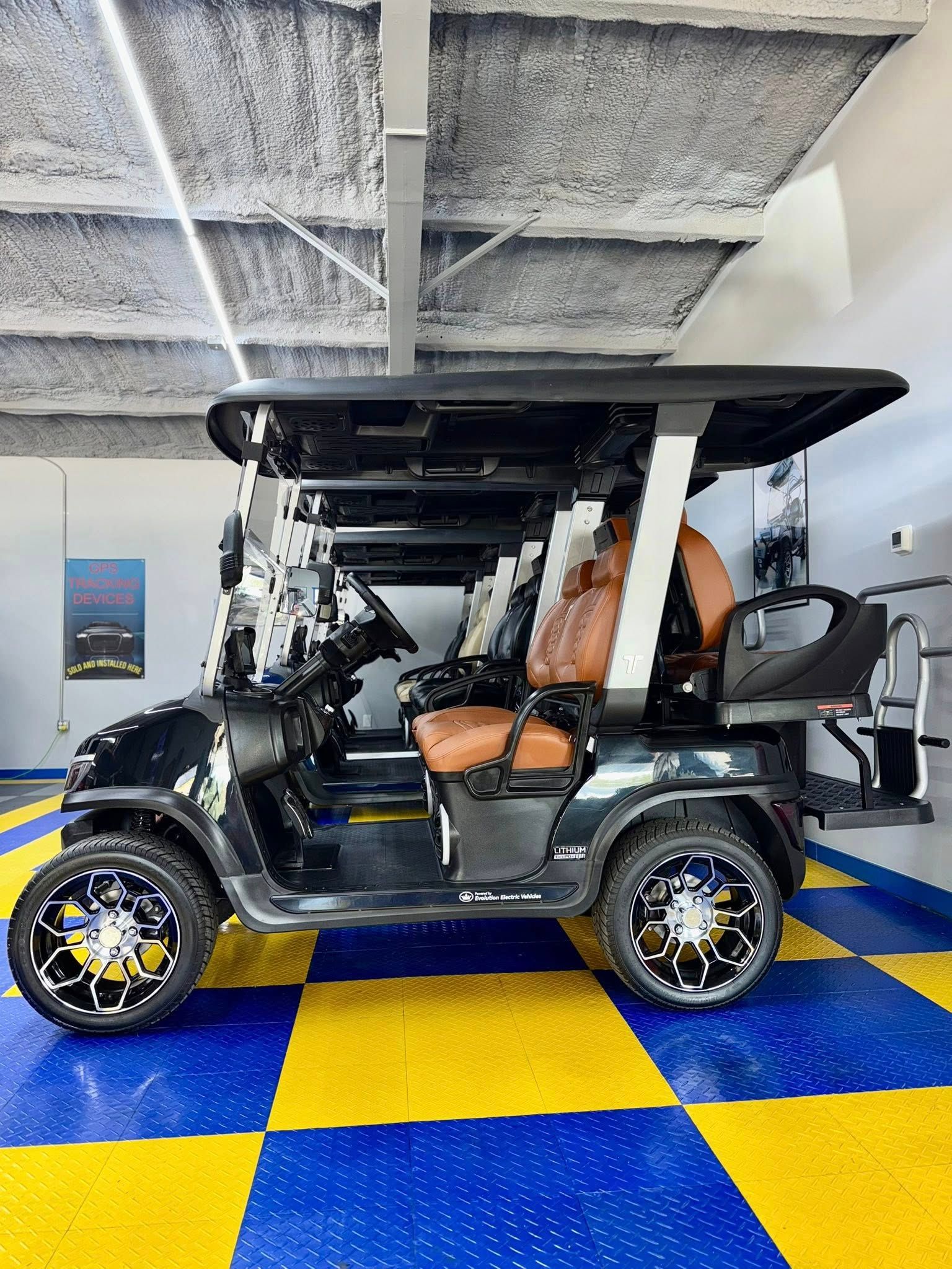 Black golf cart with brown seats and black roof parked indoors on a blue and yellow checkered floor.