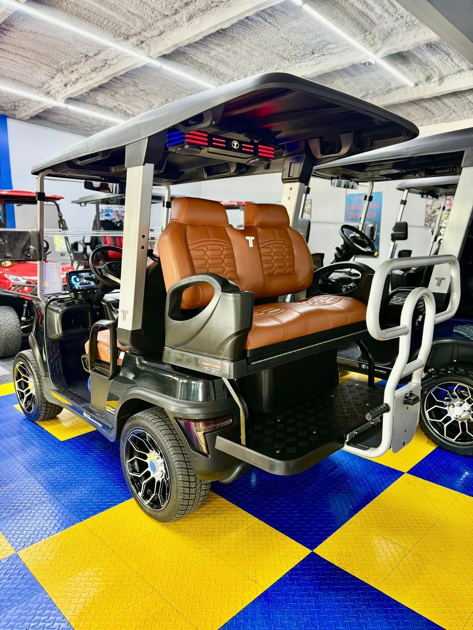 Black golf cart with brown leather seats, black rims, and a black top, parked on a checkered yellow and blue floor.