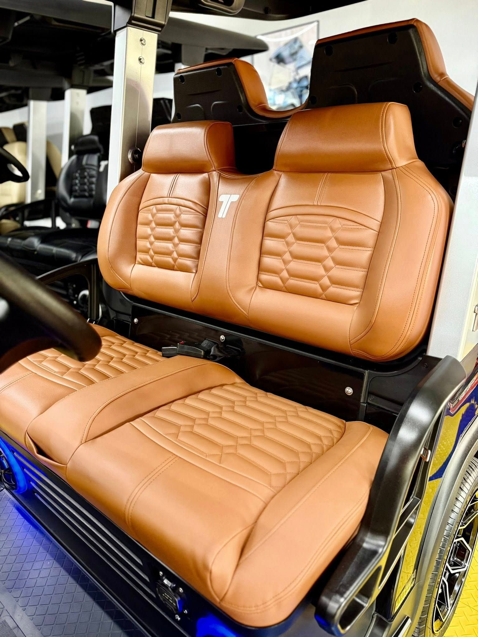 Brown leather golf cart seats with diamond stitching. The cart has a black frame, and blue LED lights are visible.