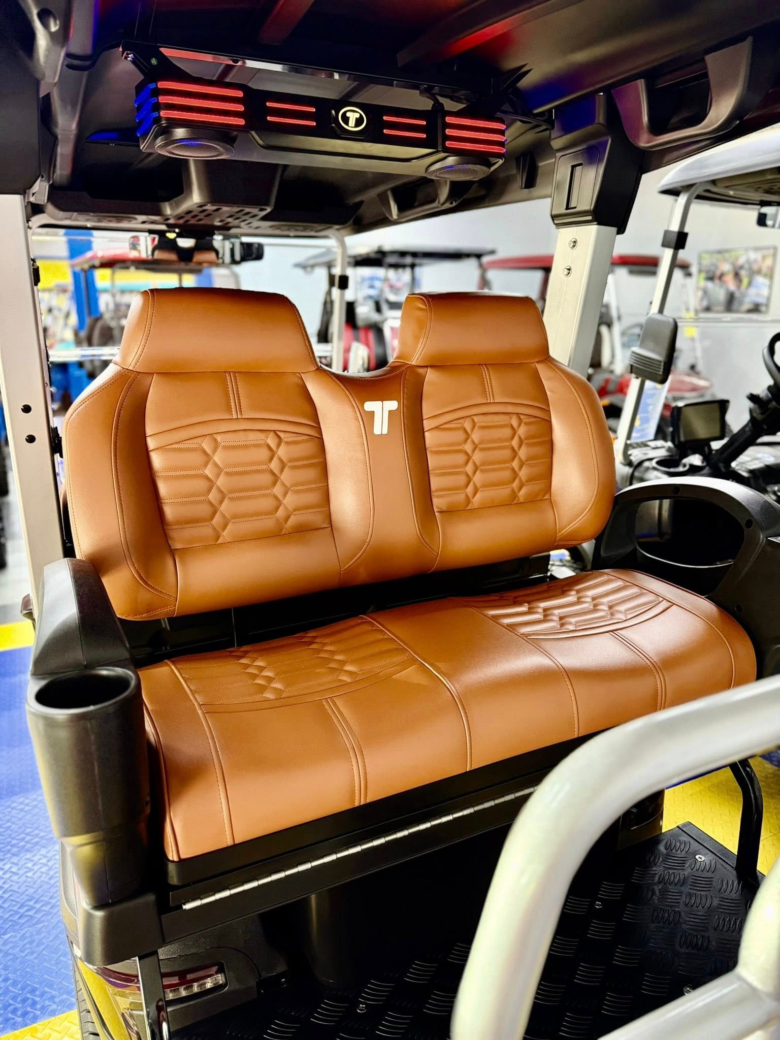 Brown leather golf cart seats with a cup holder and black trim.