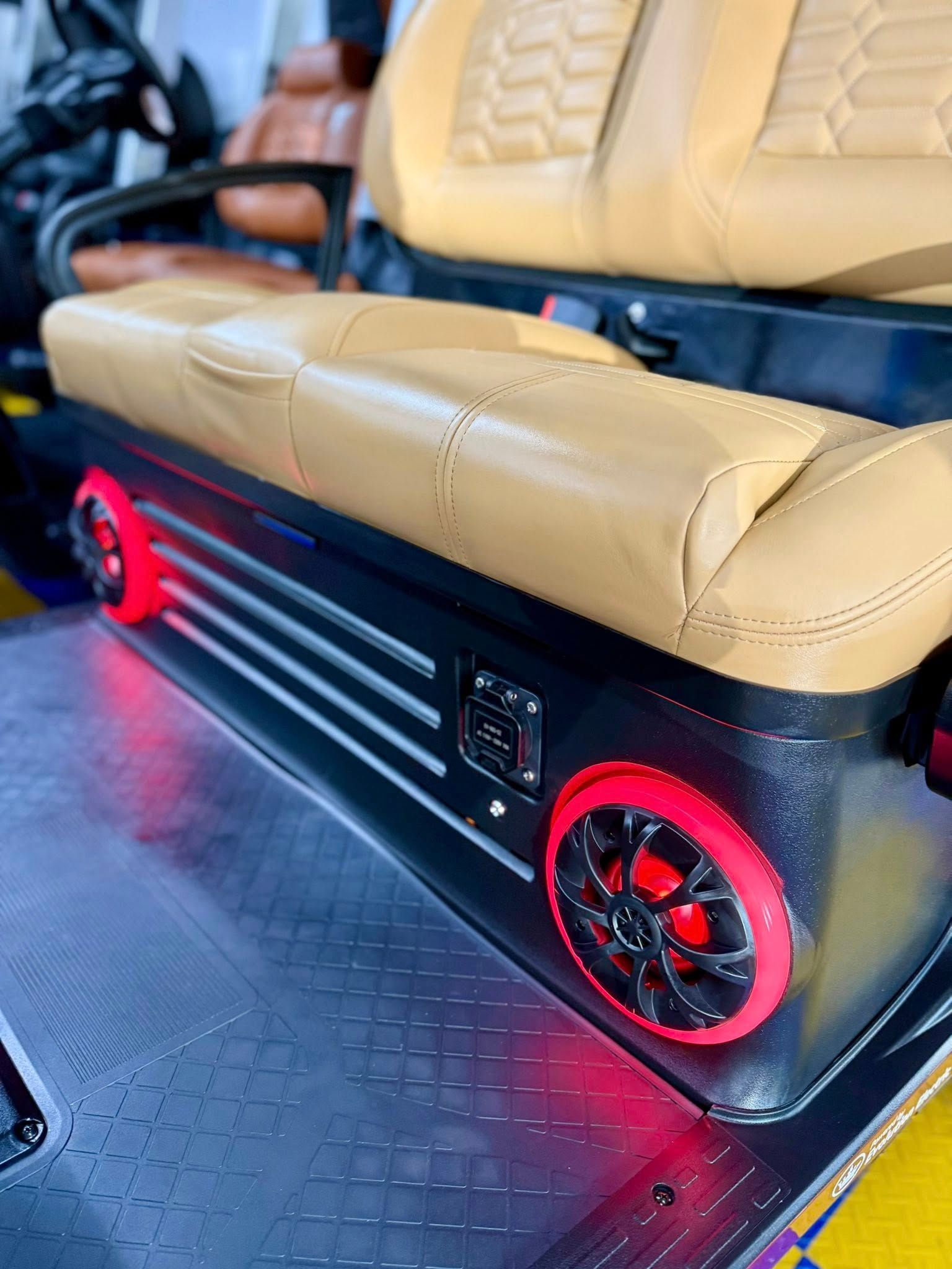 Tan upholstered seat with black trim and red-lit speakers on a vehicle.