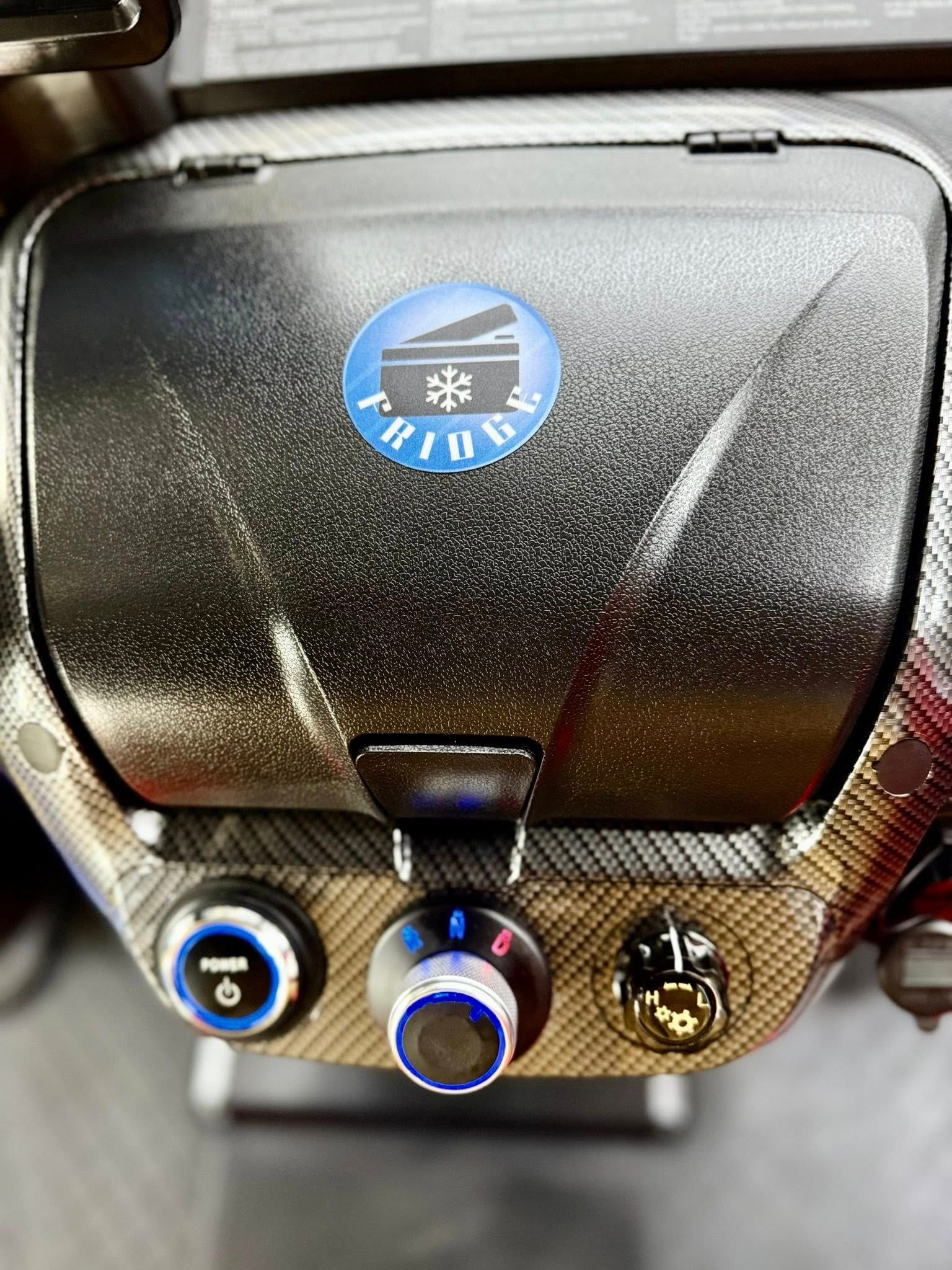 Close-up of a car's dashboard control panel with a cooling system icon, a dial, and two buttons. The panel has a patterned texture.