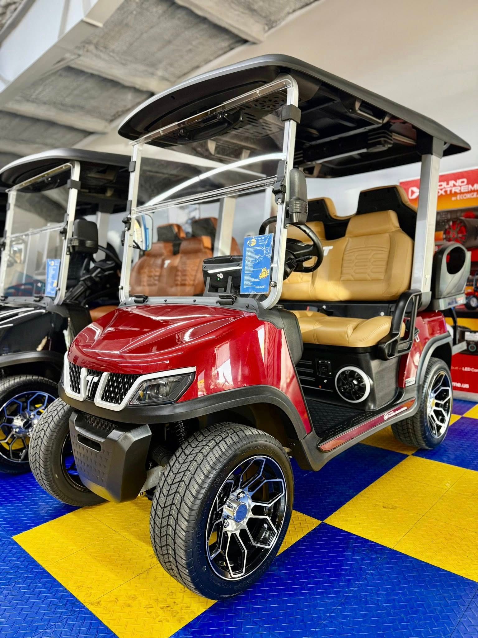 Red golf cart with tan seats, black trim, and custom wheels, parked on a checkered floor.