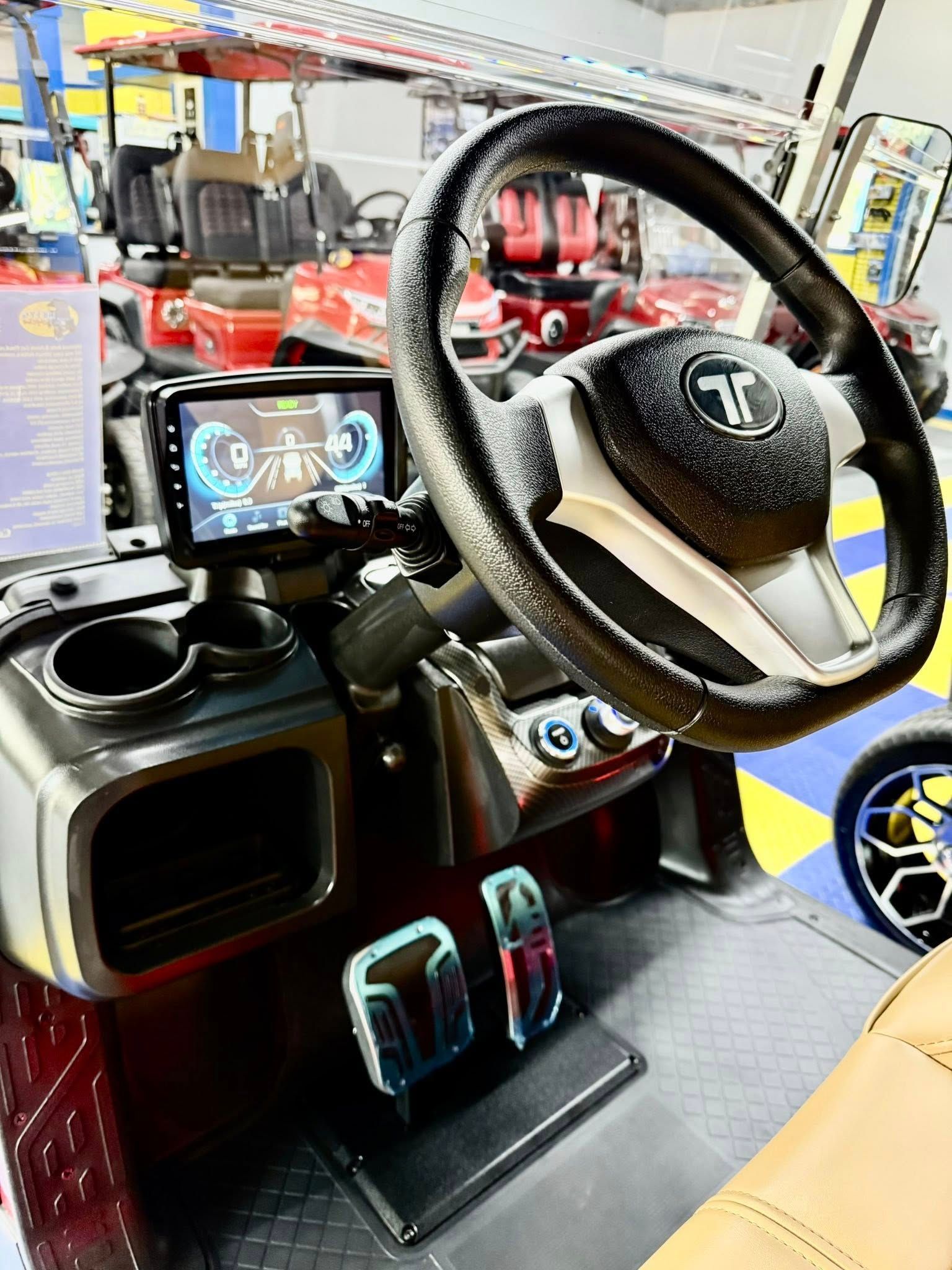 Interior of a golf cart, featuring a steering wheel, dashboard with a screen, cup holders, and pedals.