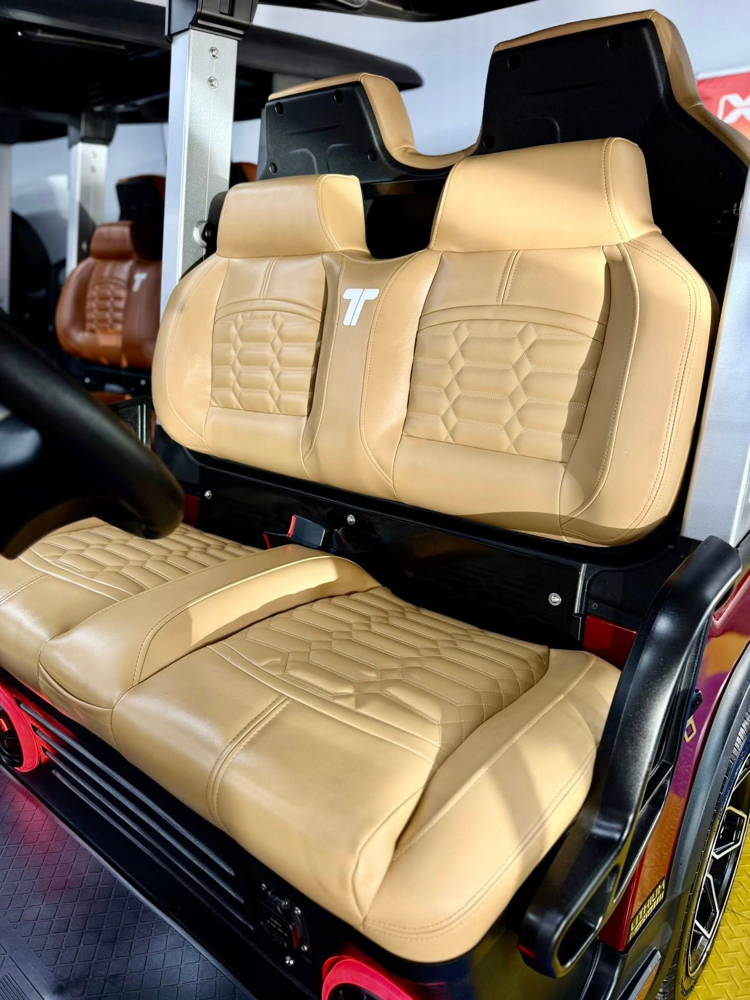 Tan leather car seats with detailed stitching in a vehicle, likely a golf cart or small buggy. Red accents on the wheels.