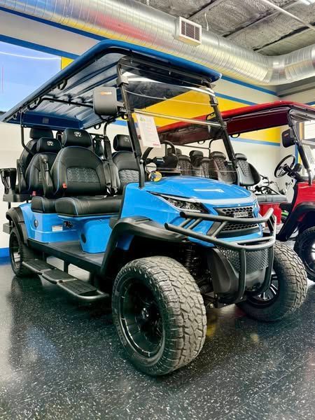 Blue golf cart with black wheels and seating displayed indoors.