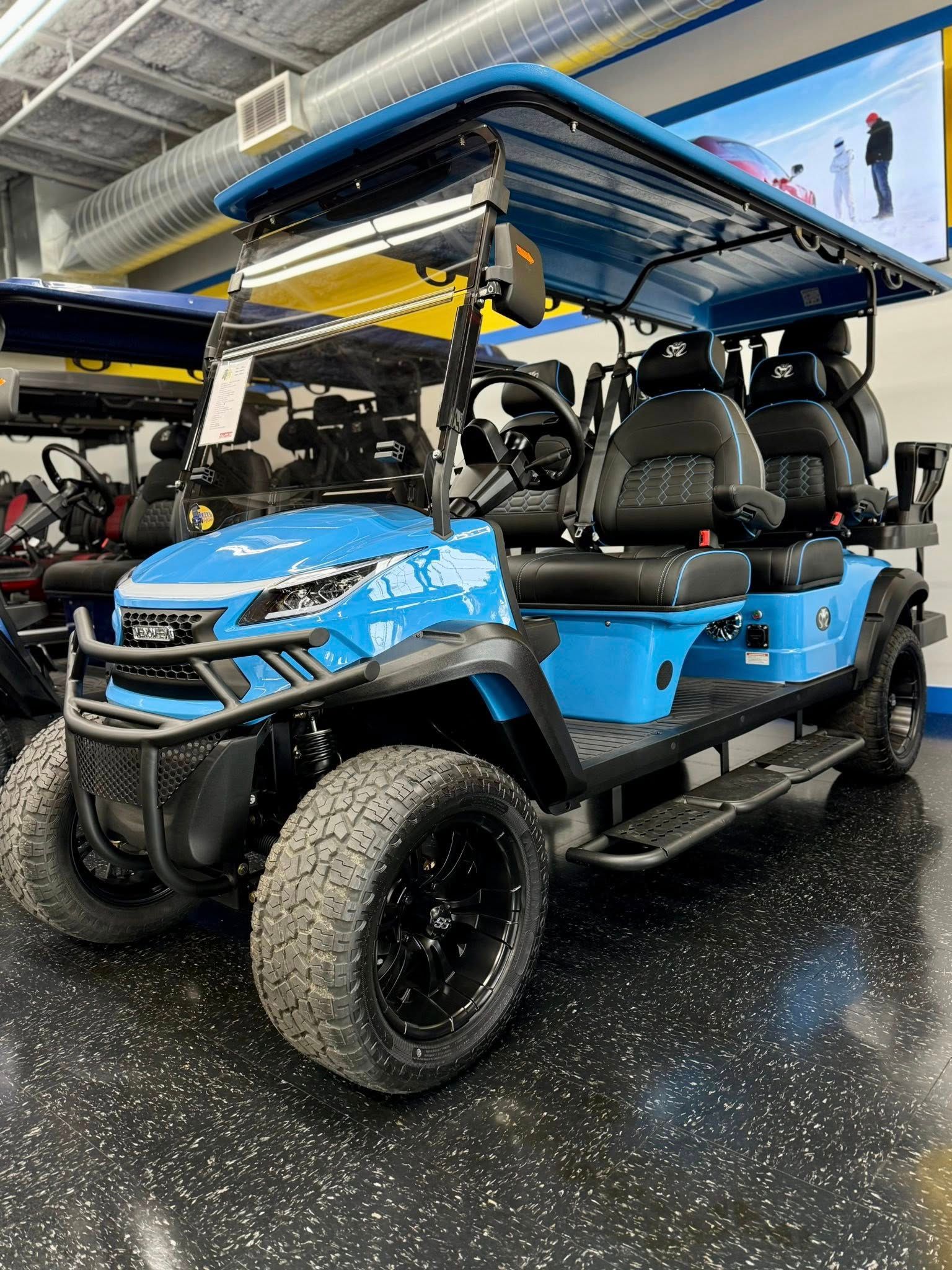 Blue golf cart with black accents and off-road tires, displayed indoors.