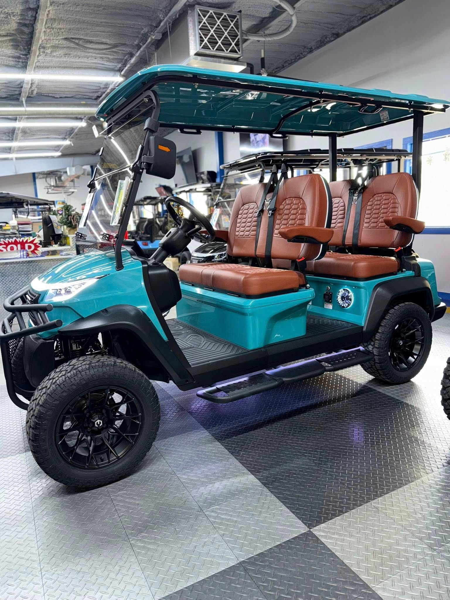 Teal golf cart with brown seats, black wheels, and a canopy. It is parked indoors.