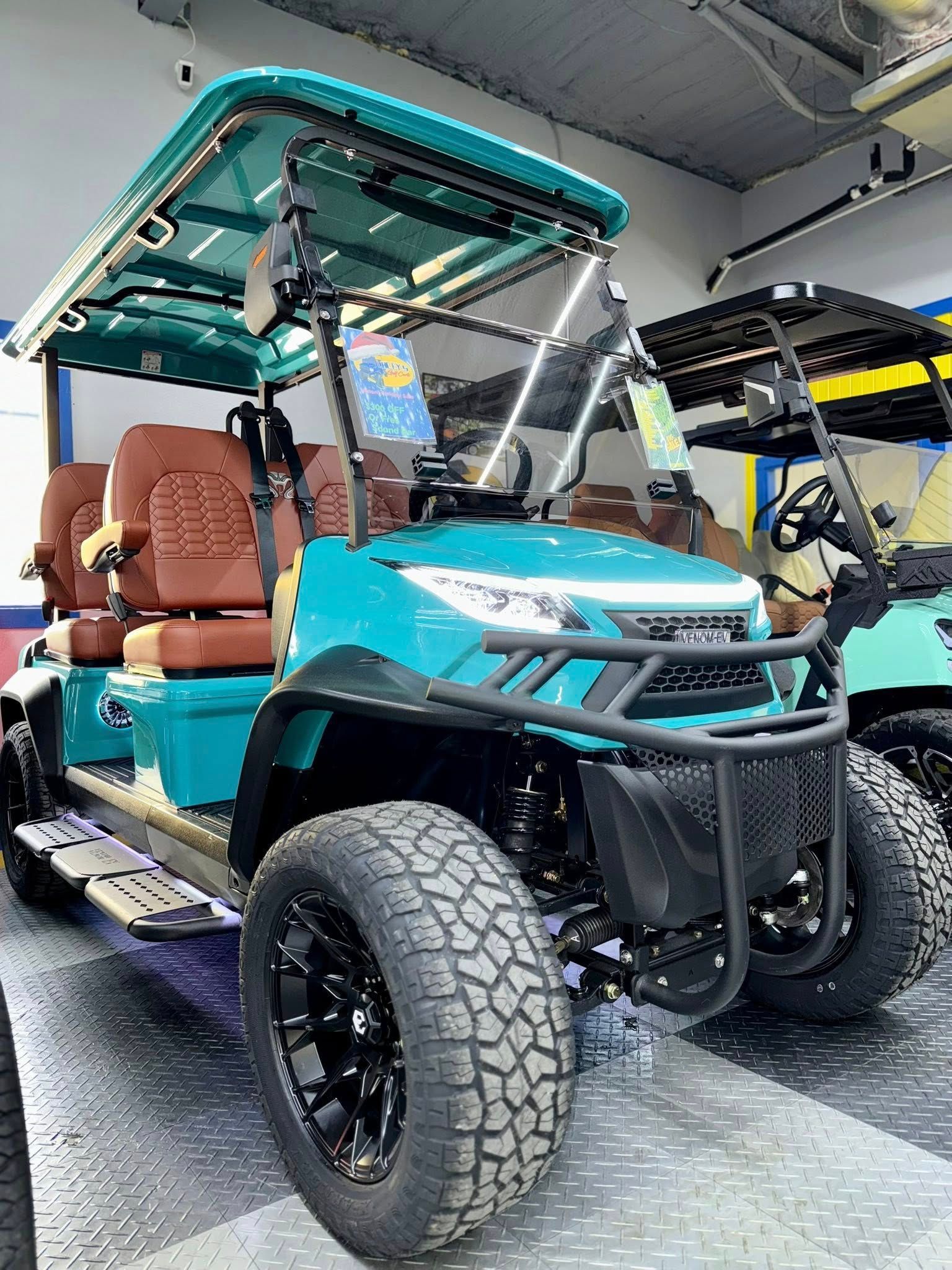 Teal golf cart with brown seats, black wheels, and off-road tires, parked indoors.