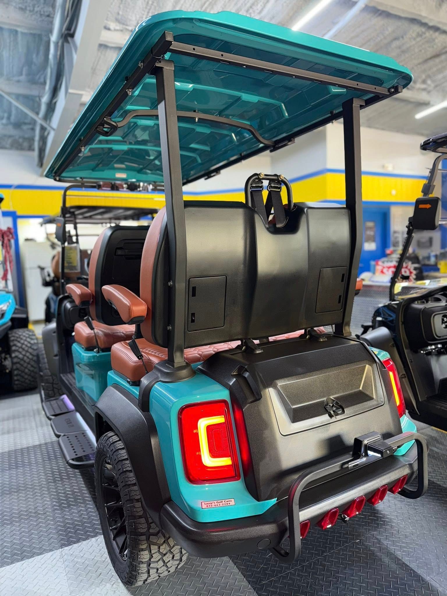 Teal and brown golf cart with a canopy. Black tires, bumper, and rear lighting. Indoor setting.