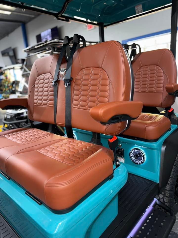 Brown and teal golf cart seats with safety belts; teal frame; black rubber floor.