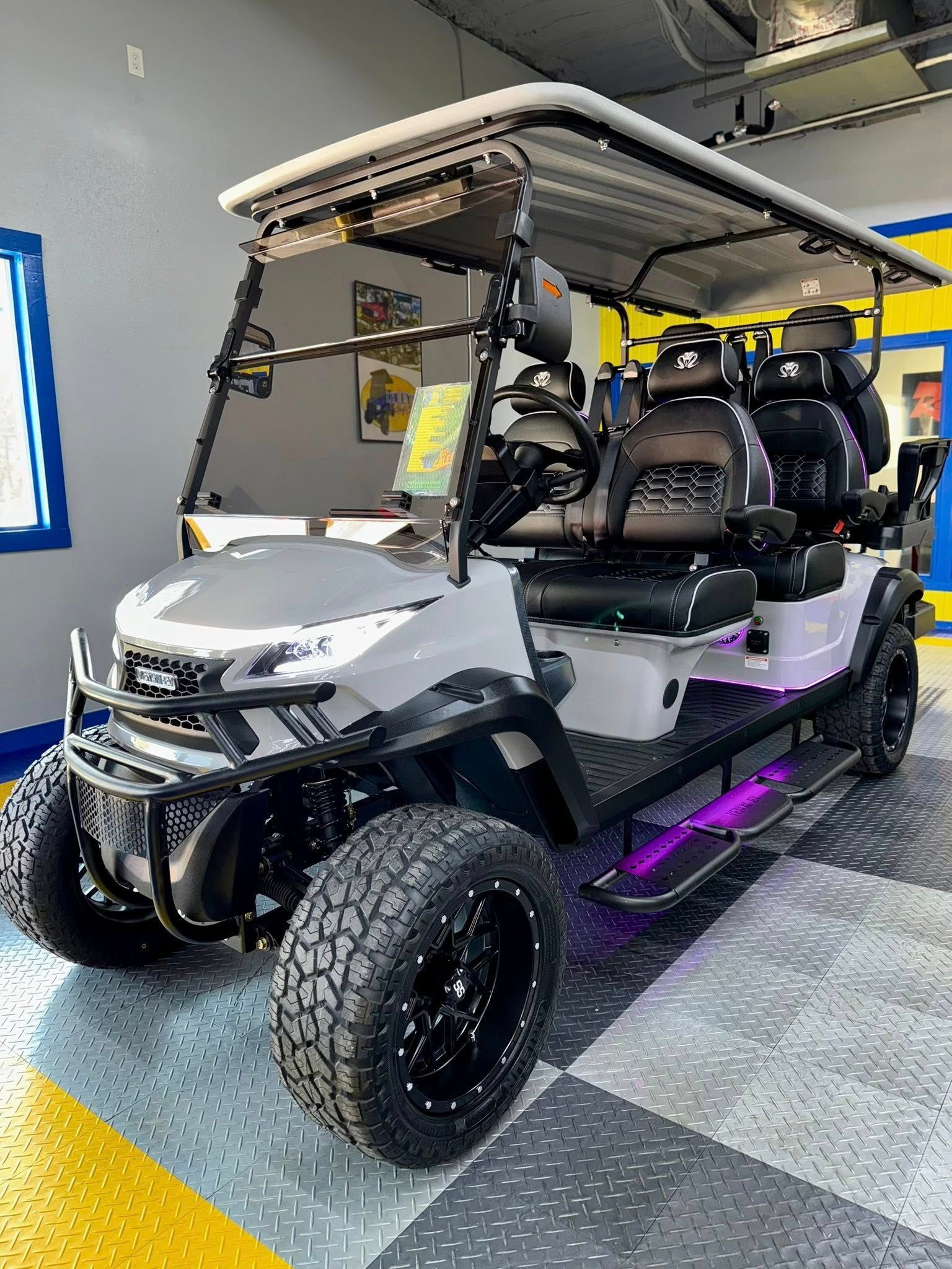 Grey and black customized golf cart with off-road tires, LED lights, and black seats inside a garage.