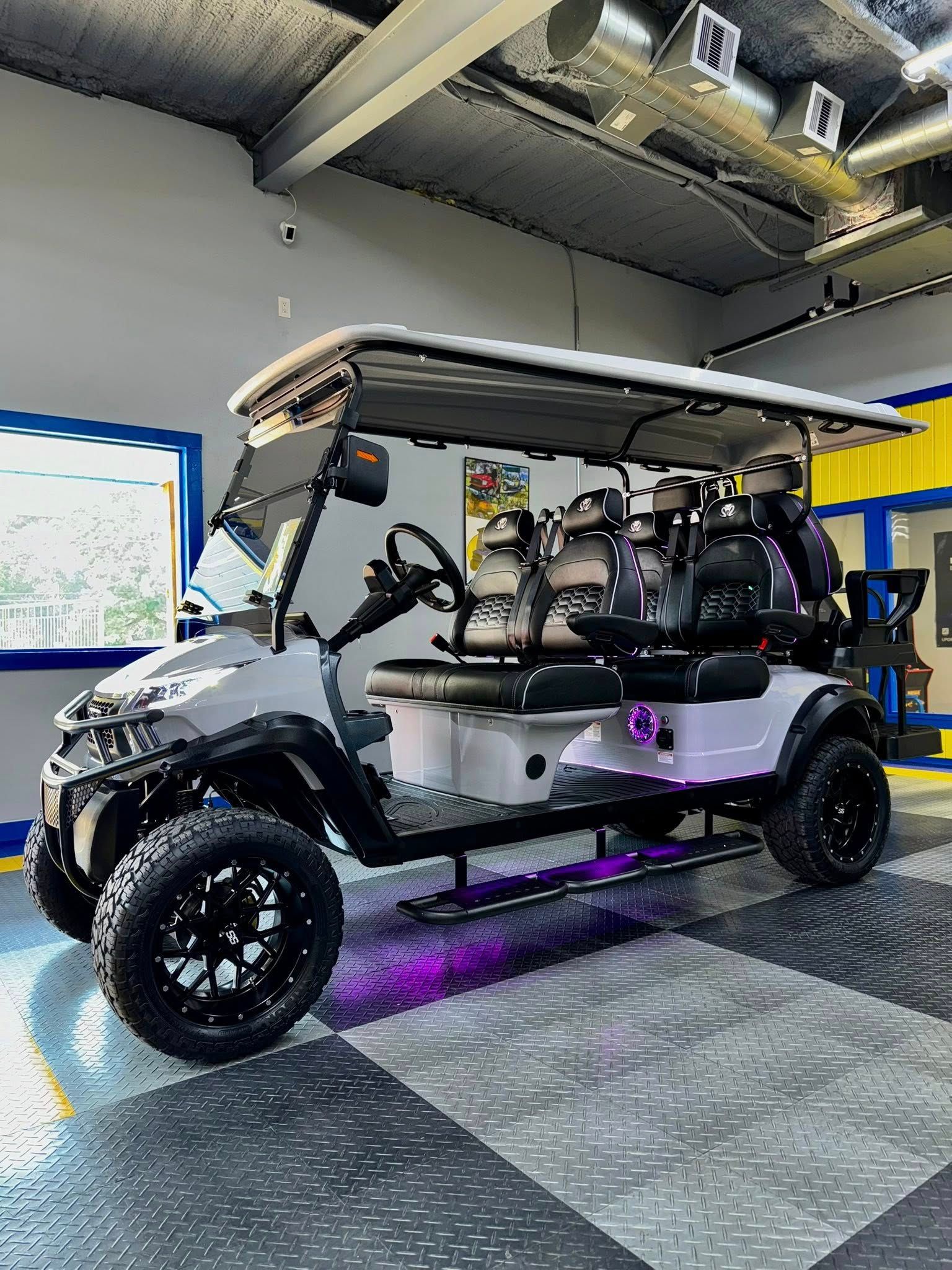 Customized gray golf cart with black wheels and purple underglow lights, indoors.
