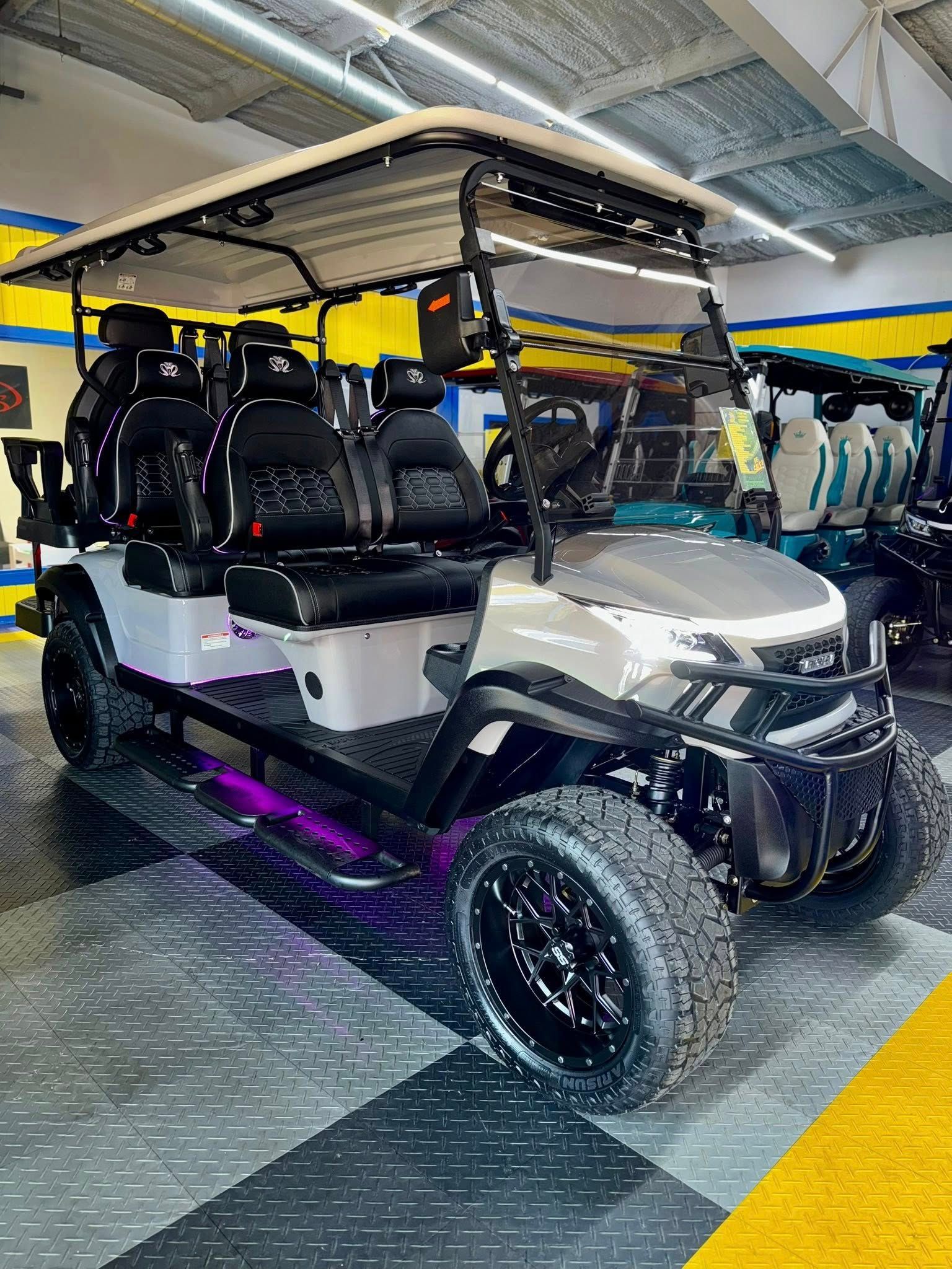 Gray and black golf cart with custom wheels and purple underglow, in a showroom.