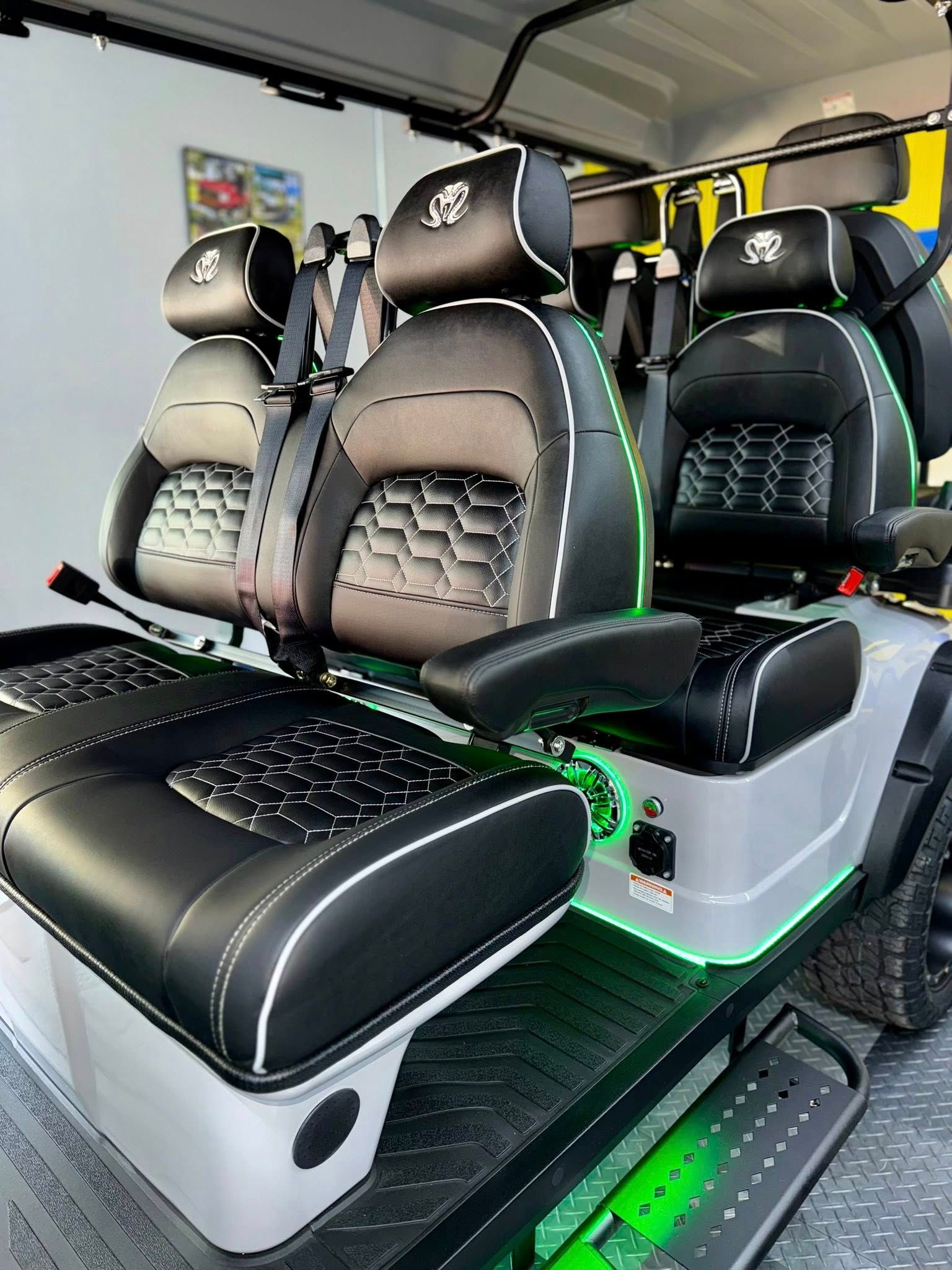 Custom golf cart with black and gray seats, green accents, and a roll cage.