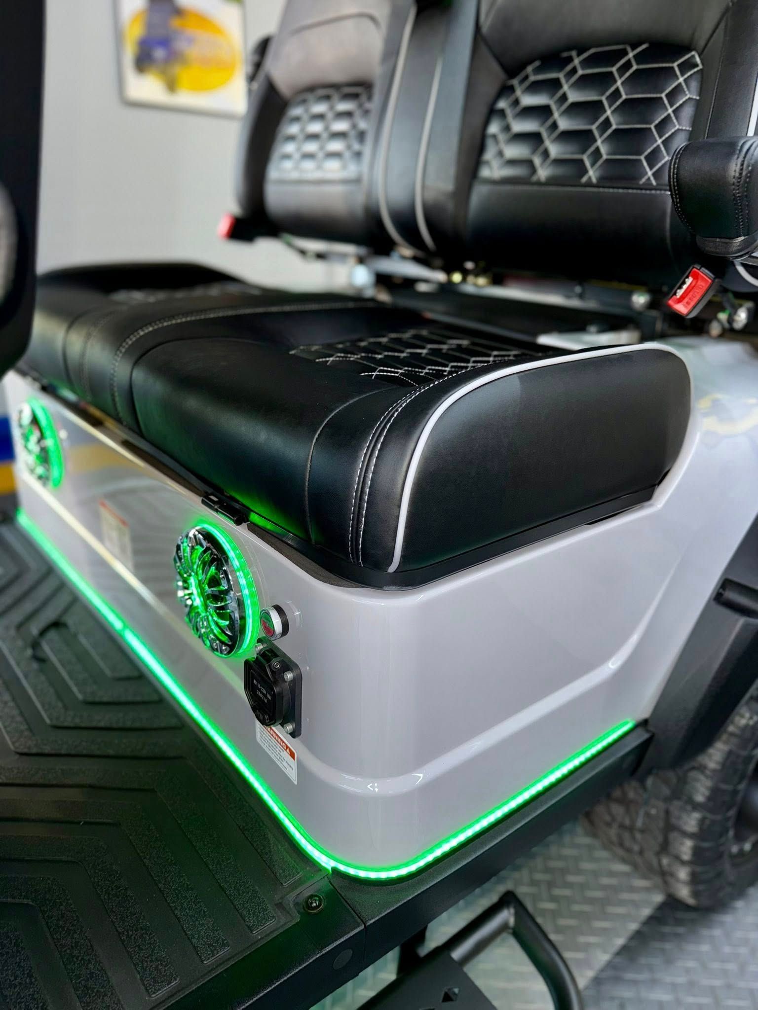 Golf cart interior with black and gray seats, speakers, and green LED lighting.