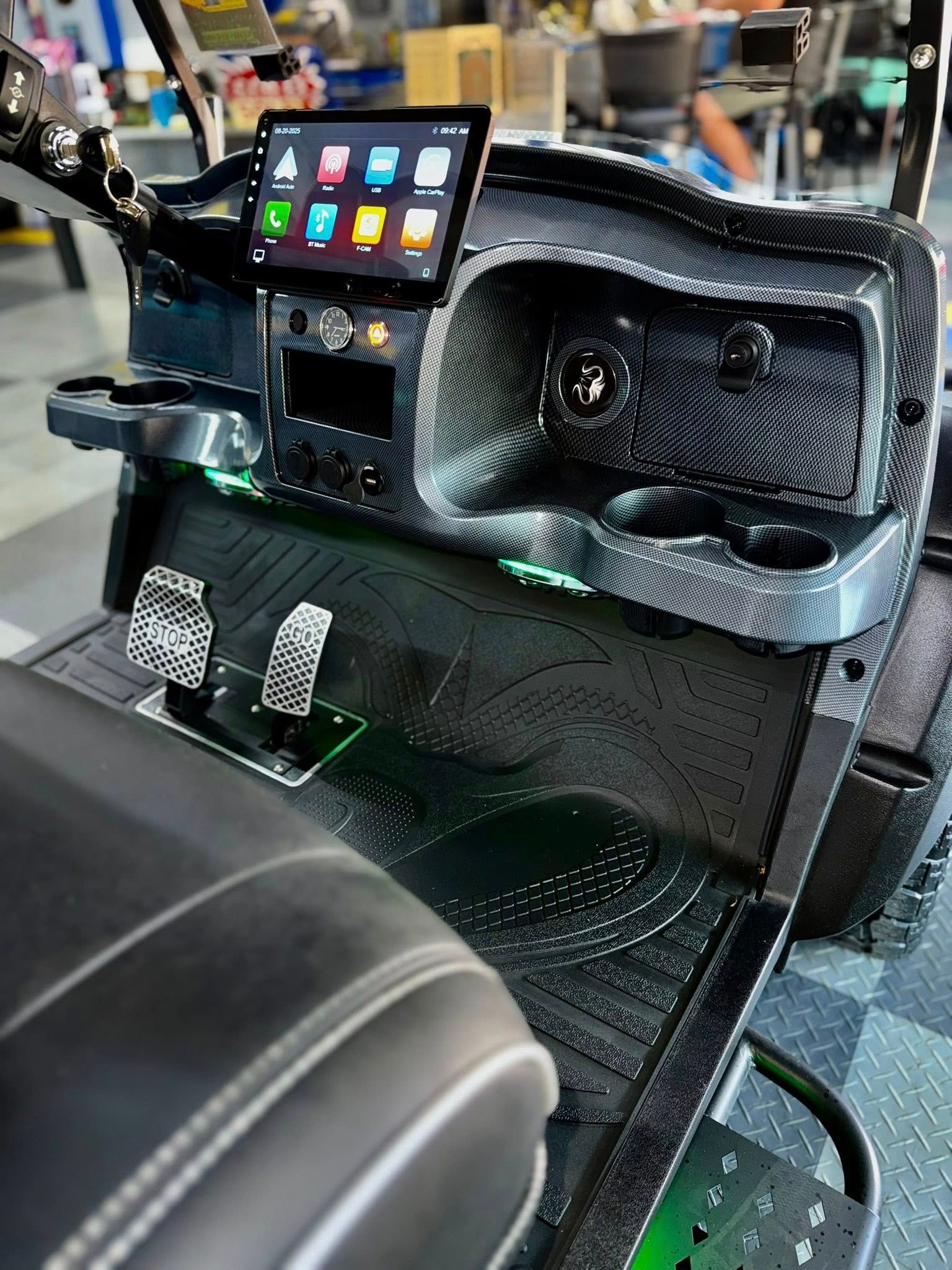Customized golf cart interior with a digital display, cup holders, and textured black surfaces.