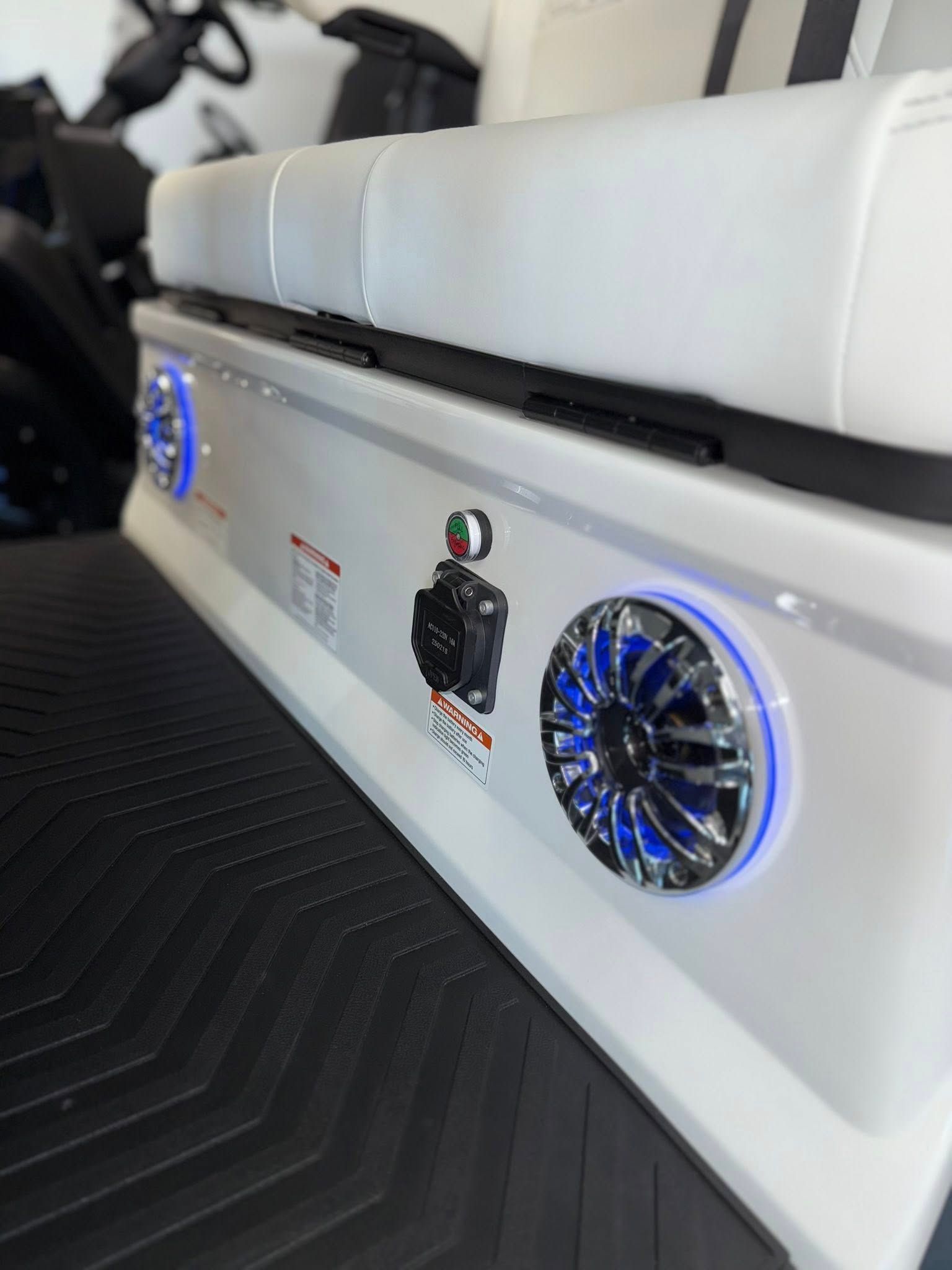 White golf cart rear with speakers and blue lights, next to seat and black textured floor.