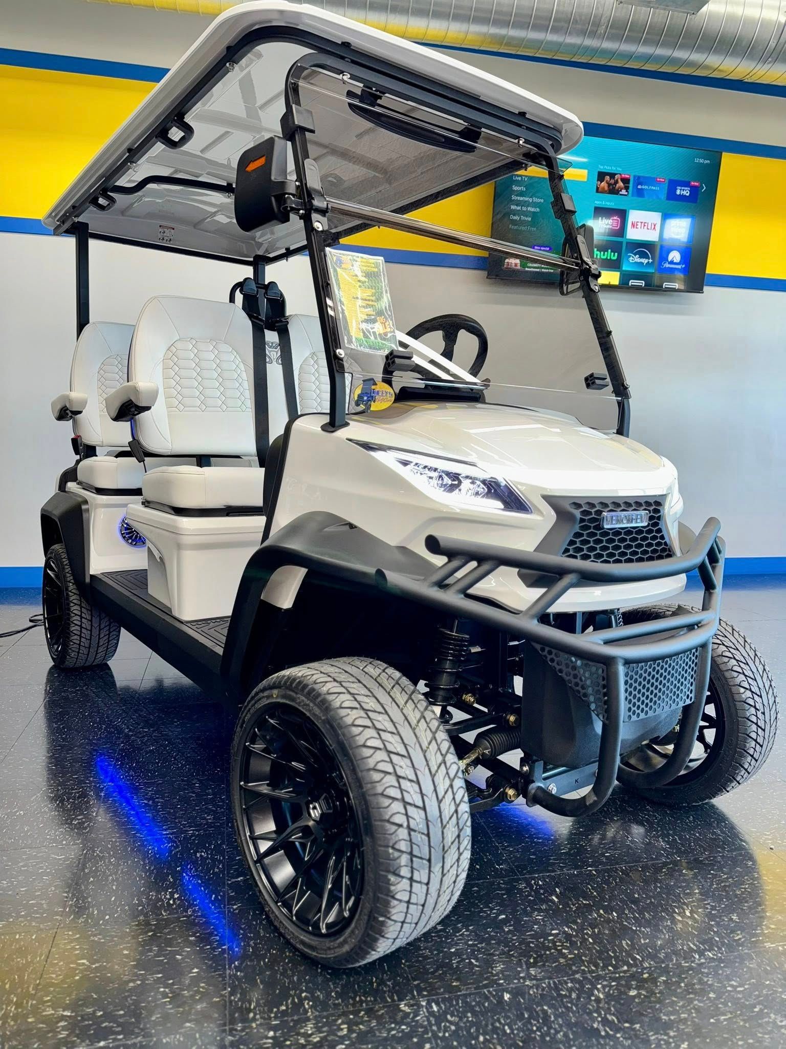 White golf cart with black accents, lifted wheels, LED lights, and a canopy in a showroom.