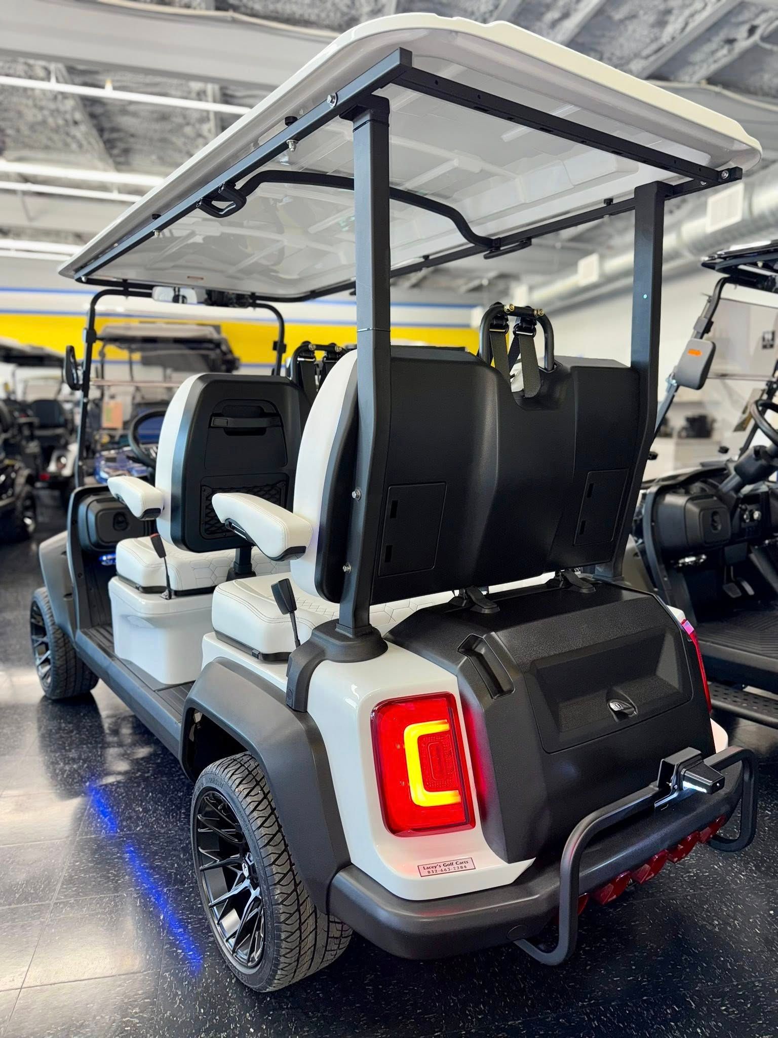 White and black golf cart with four seats, black wheels, and a rear storage compartment.