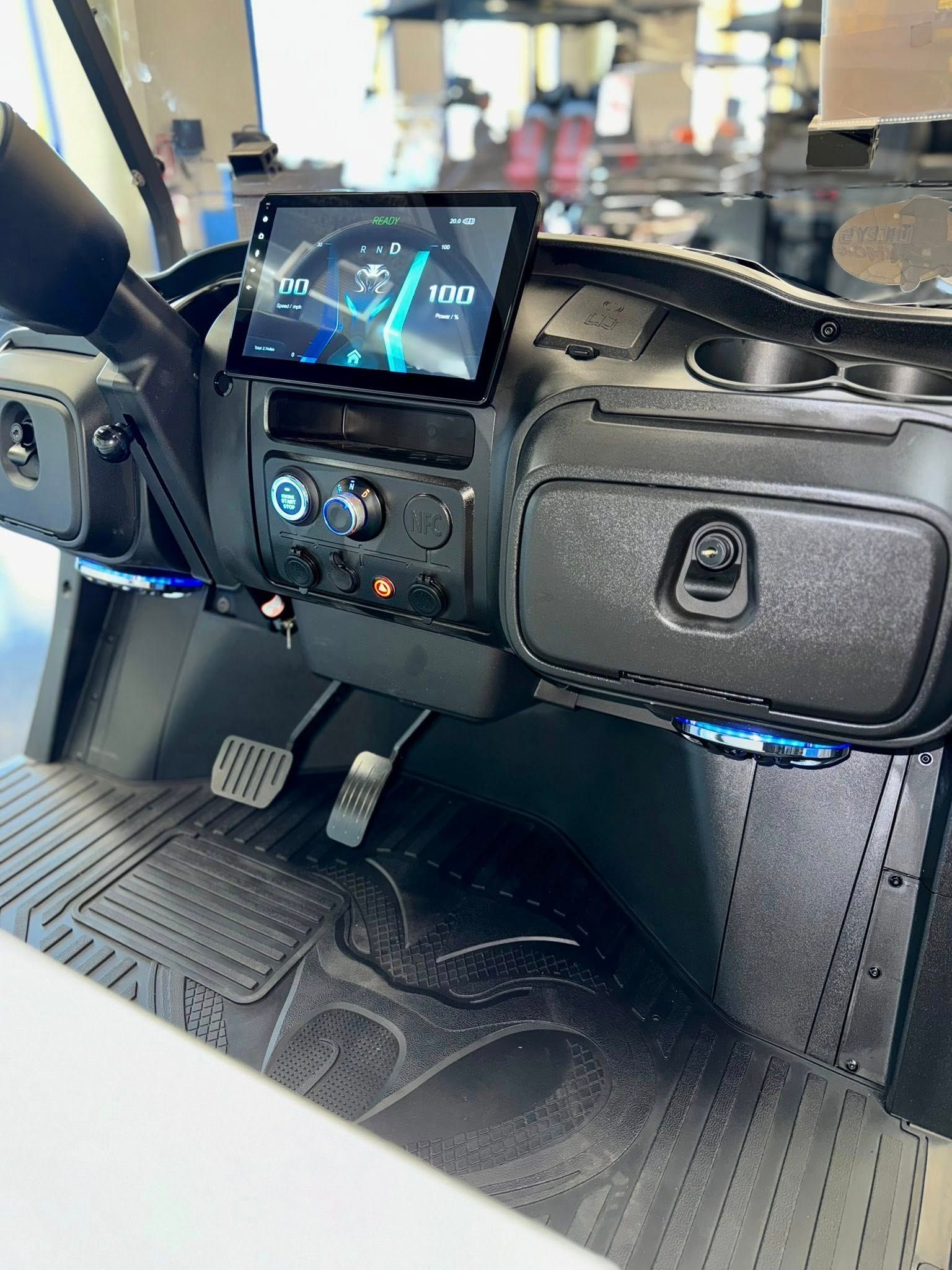 Interior of a golf cart dashboard with a digital display, buttons, storage, and blue lights.