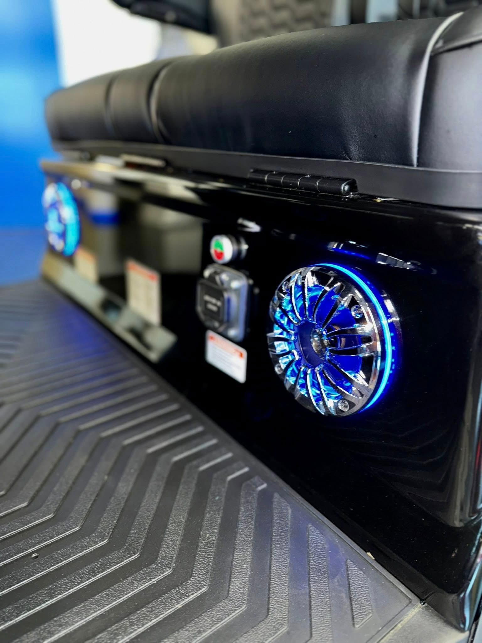 Black golf cart rear with lit blue speakers, power outlets, and black seats.