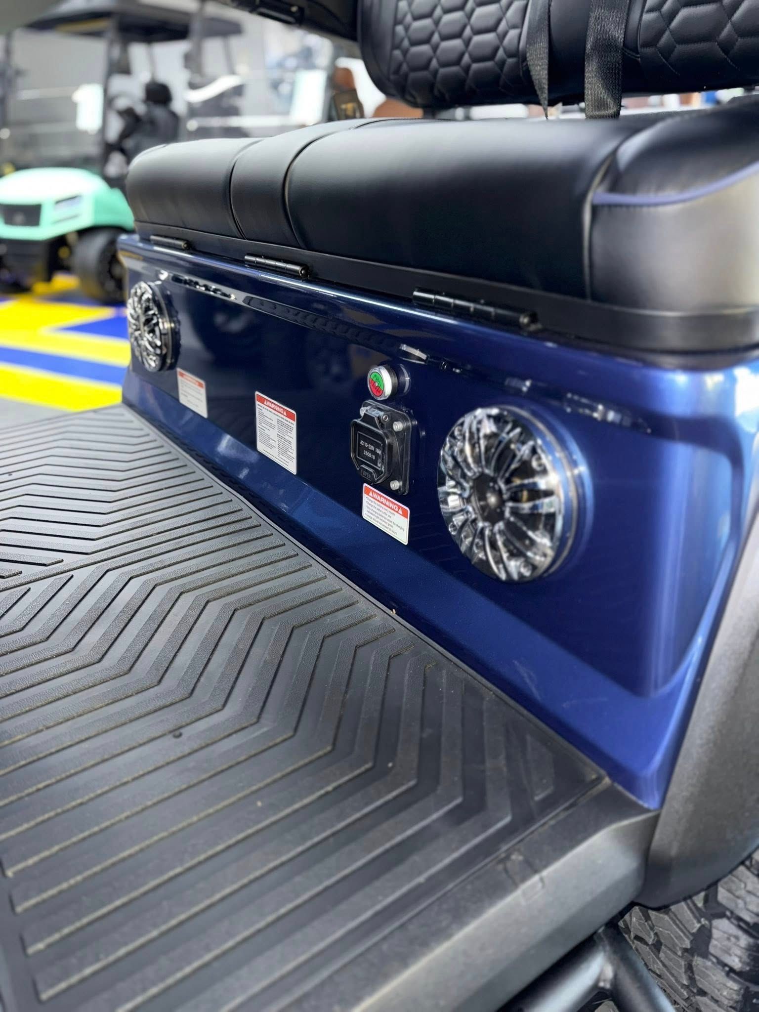 Blue golf cart's rear panel with speakers, controls, and black textured floor.