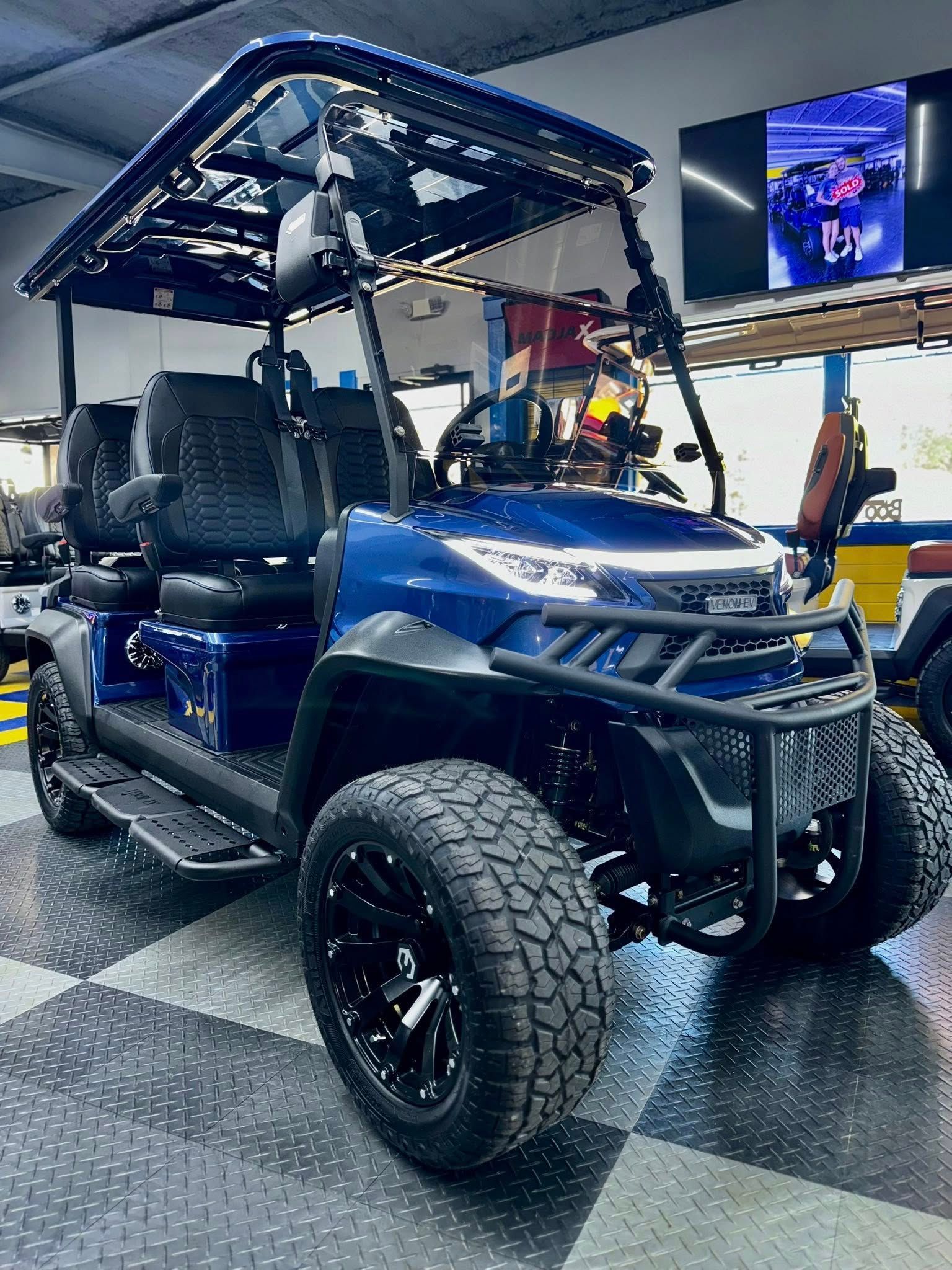 Blue lifted golf cart with black wheels, roof, and brush guard in a showroom.