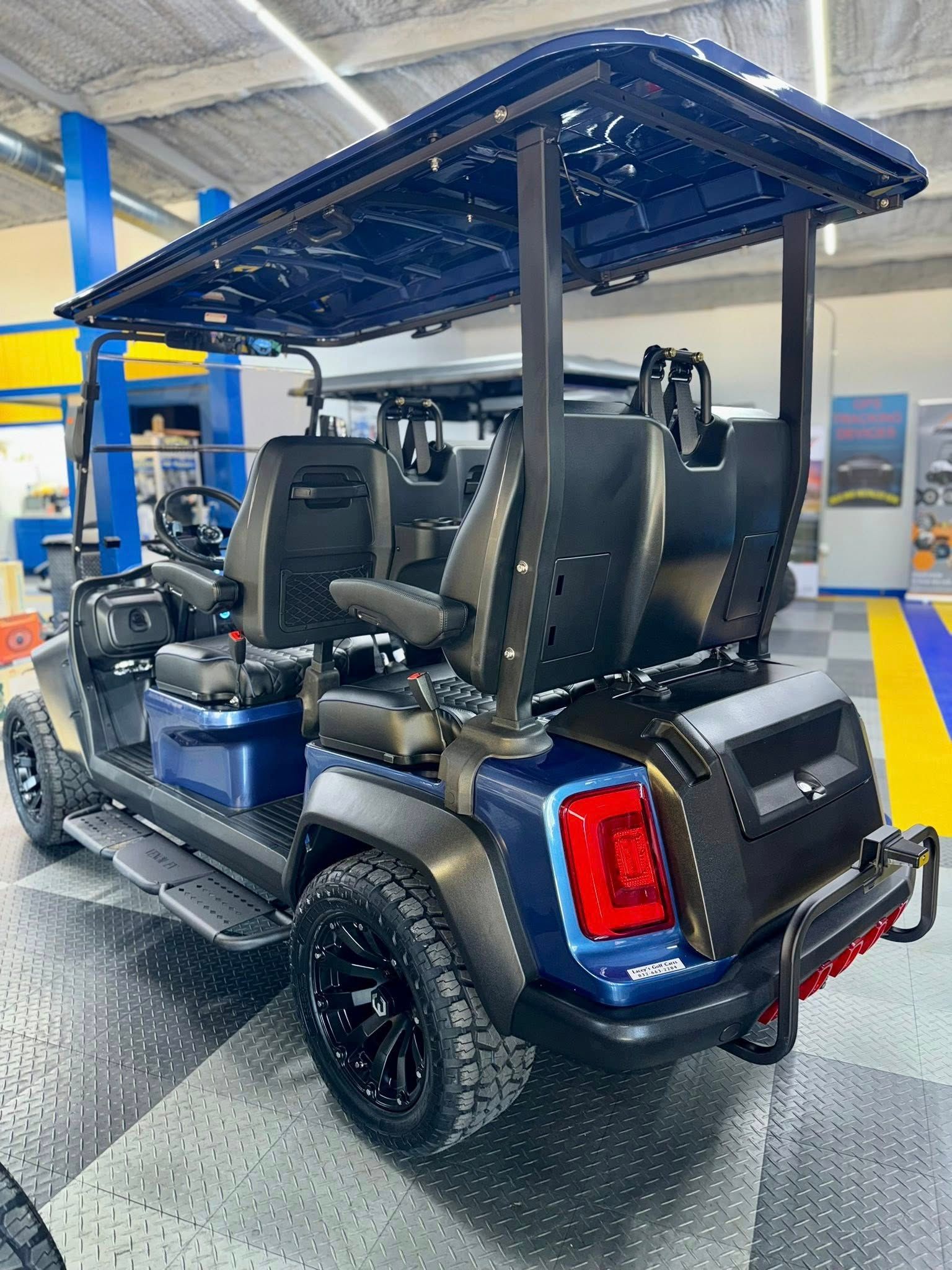 Blue golf cart with black roof, seats, and wheels, parked inside.