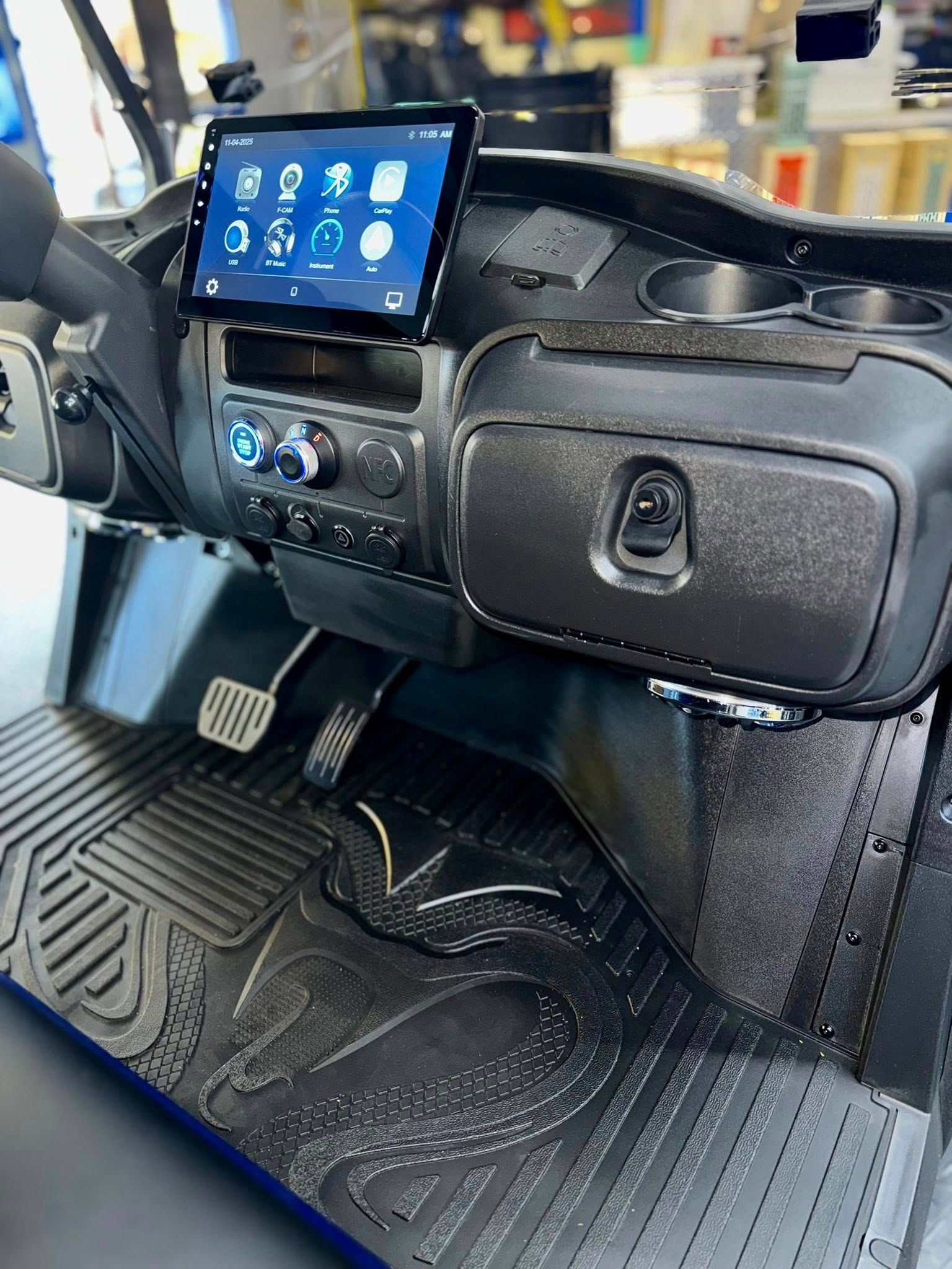 Black golf cart dashboard with a digital screen, storage compartments, and textured floor mat.