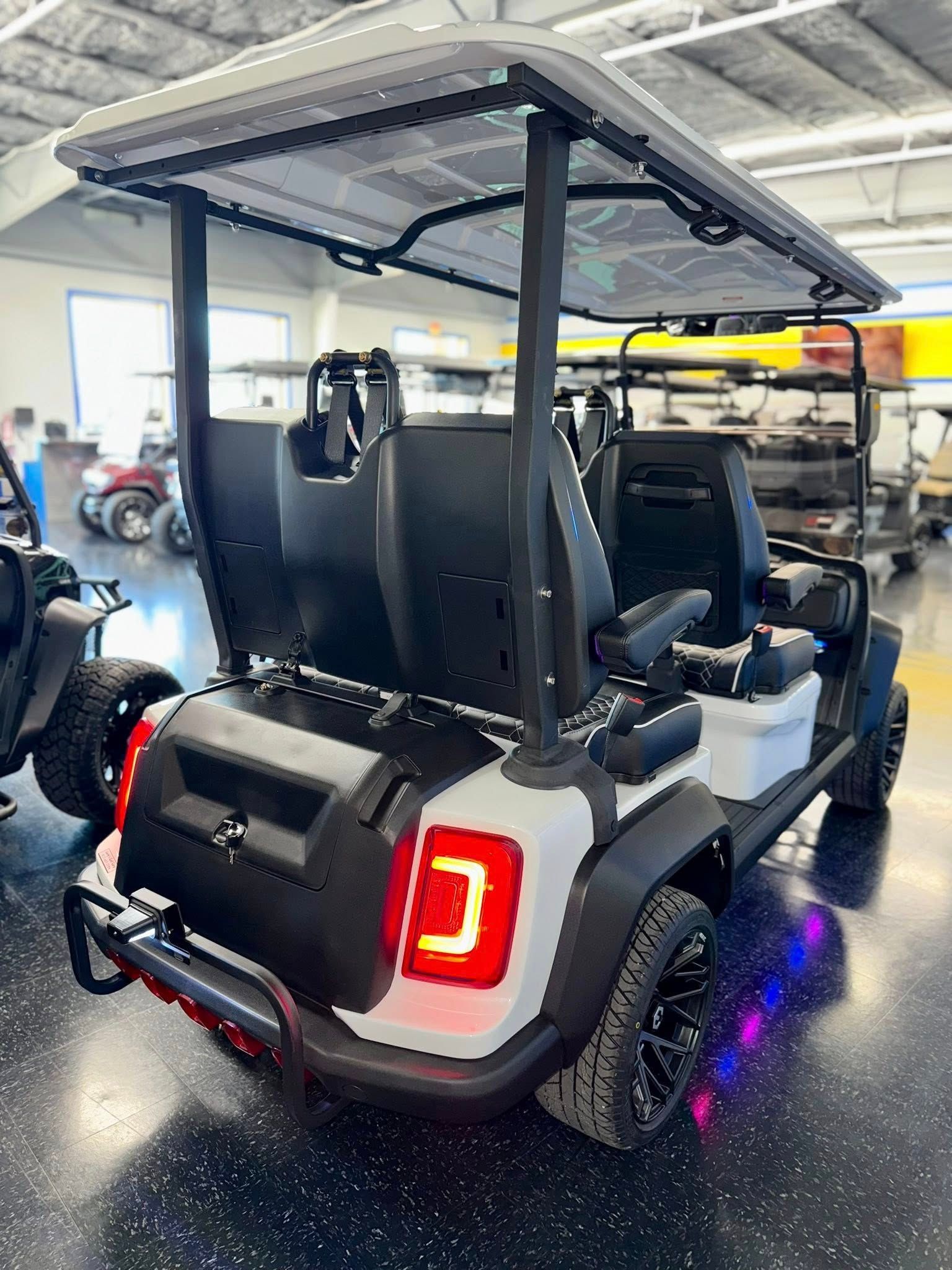 White and black golf cart with canopy, black wheels, and bright tail lights in a showroom.