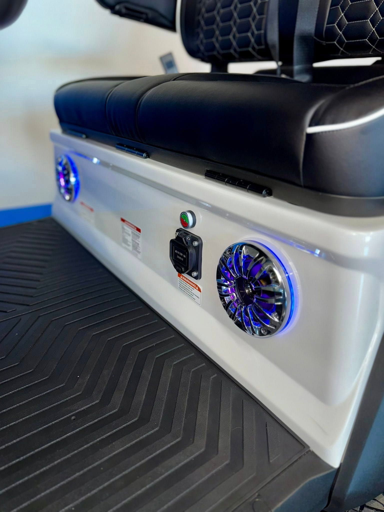 Golf cart with white body, speakers with blue lights, black seats, and control panel.
