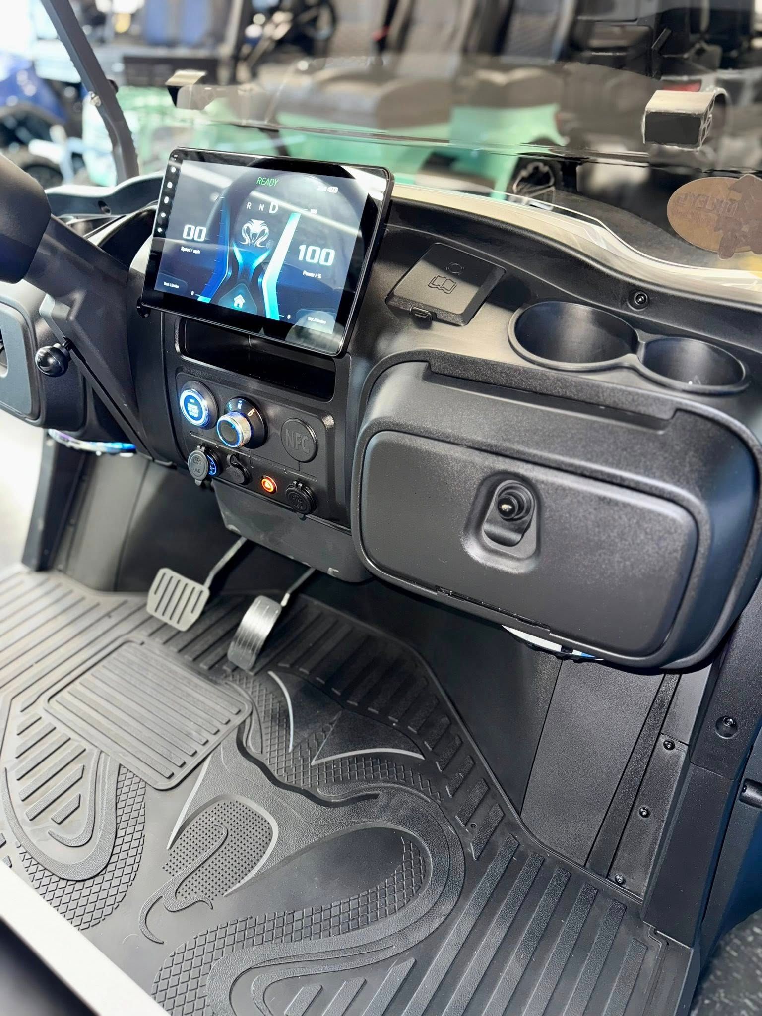 Interior of a black golf cart dashboard with a screen, cup holders, and storage compartment.