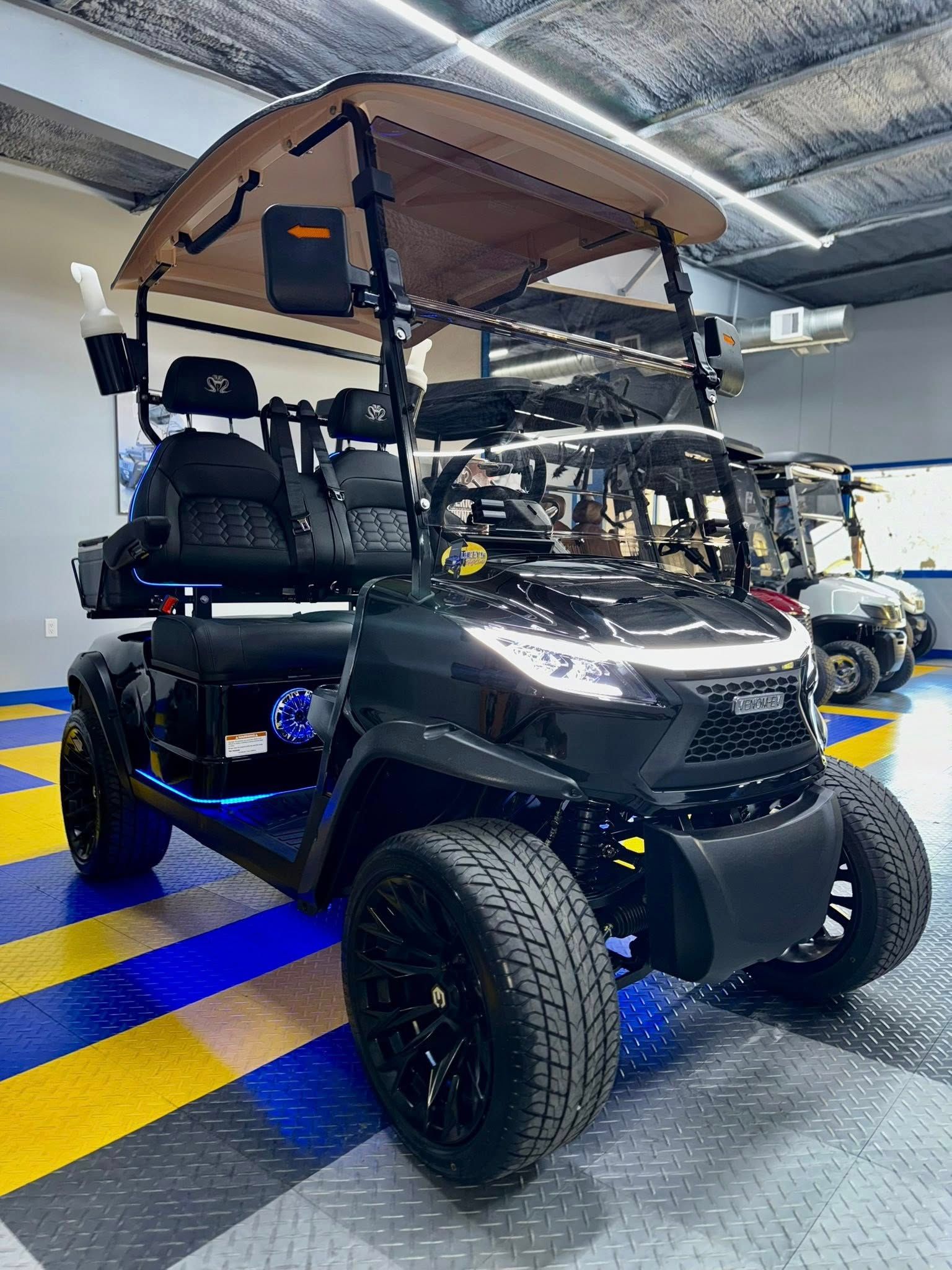 Black golf cart with lifted suspension, tan roof, and black seats, inside a garage.