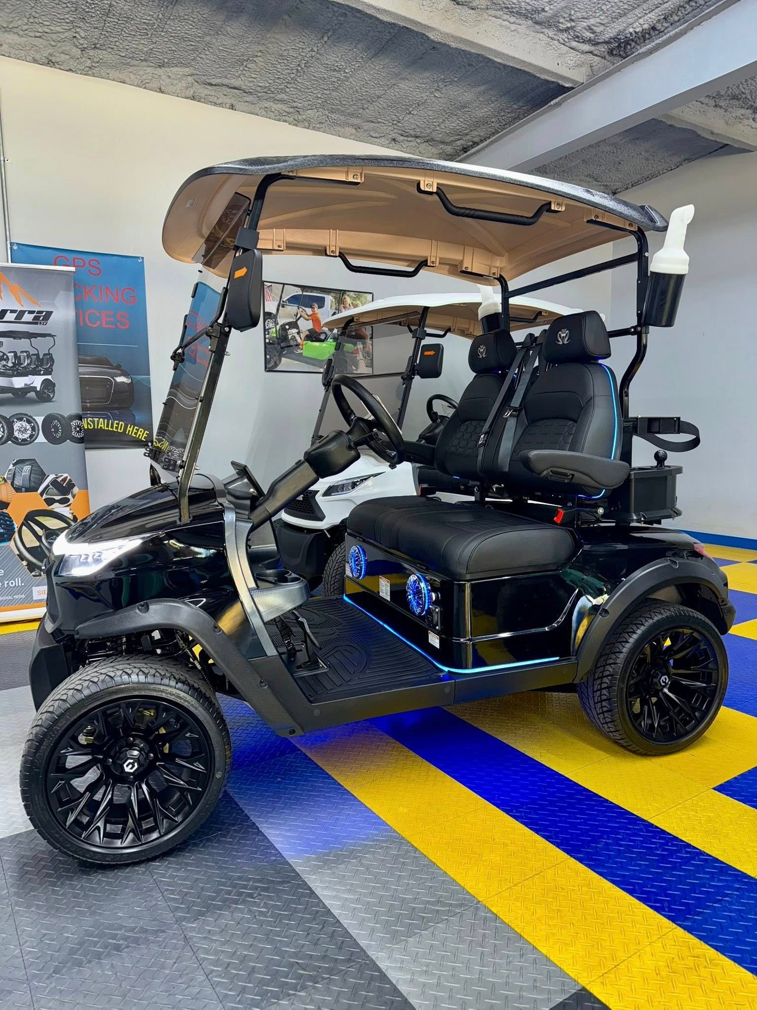 Black golf cart with black wheels, seats, and a tan top, parked on a blue and yellow tiled floor.